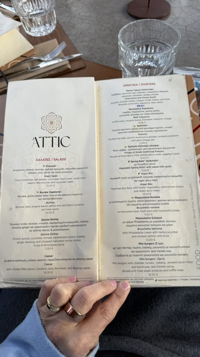 A hand holding open the menu at Attic Urban Rooftop, with glasses on the table behind