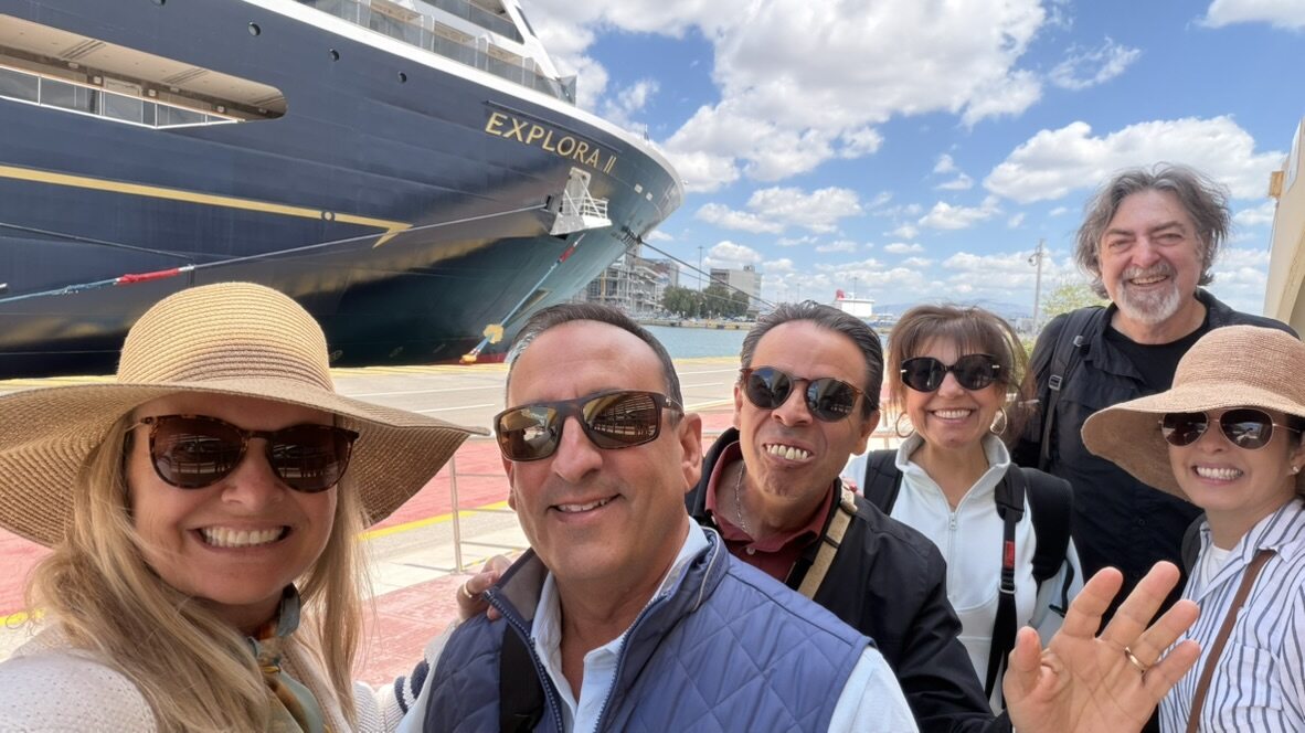 The group of friends in sun hats taking a selfie on the dock in front of the Explora II hull at Piraeus