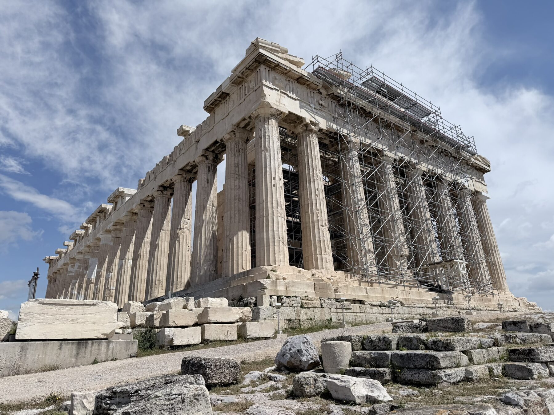 The Parthenon on the Acropolis under a blue sky with white clouds, scaffolding visible on one end