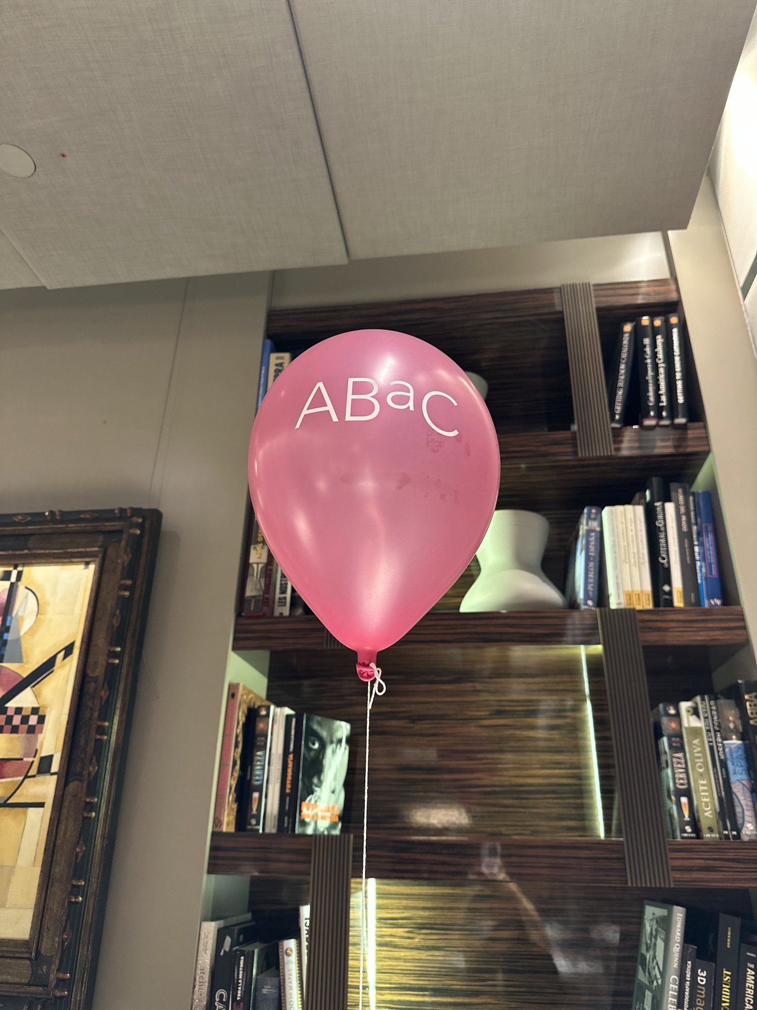 A pink balloon printed with ABaC floating in front of a bookshelf