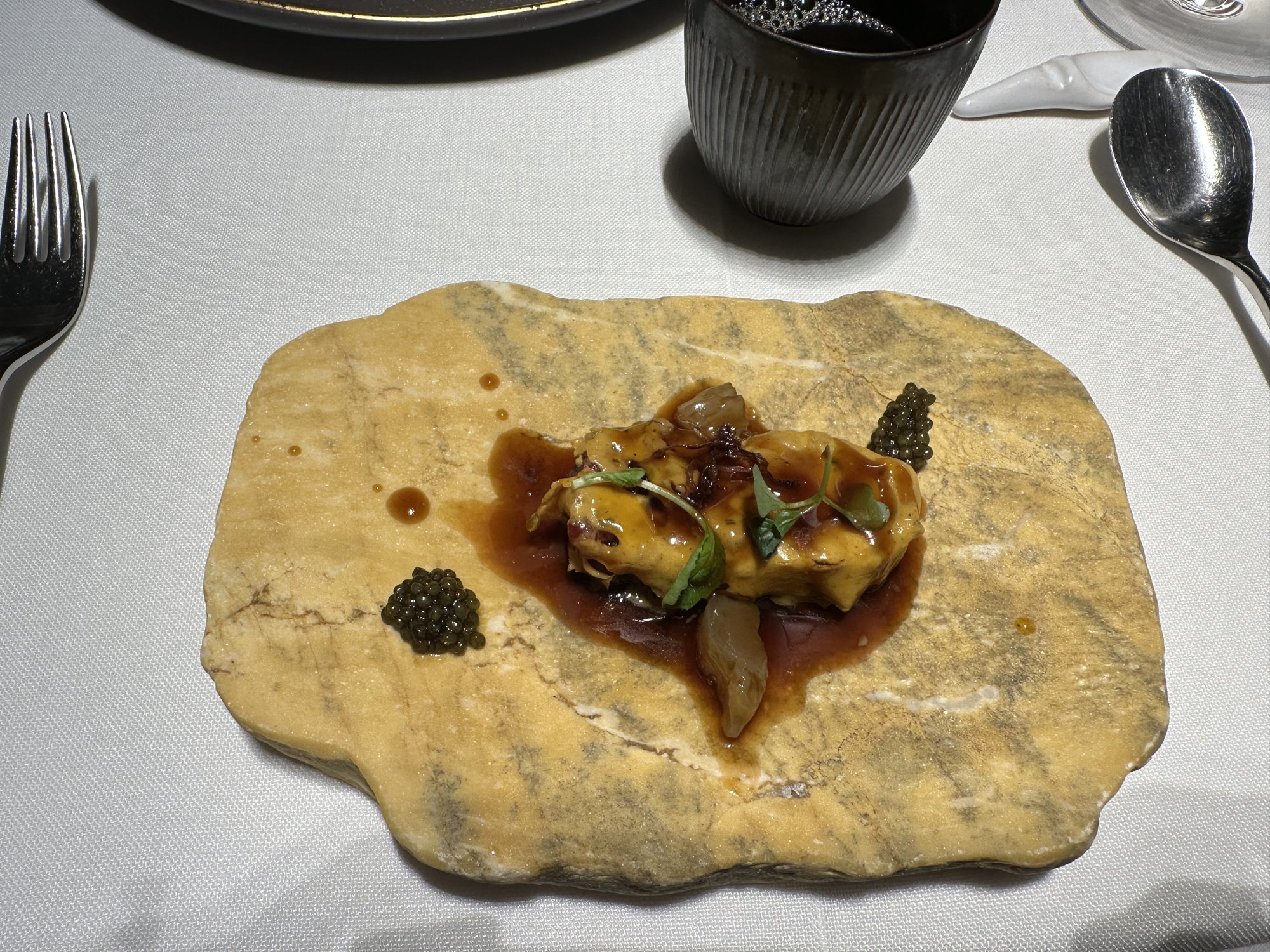 A seafood dish in dark sauce with a quenelle of caviar on a pale flat stone plate