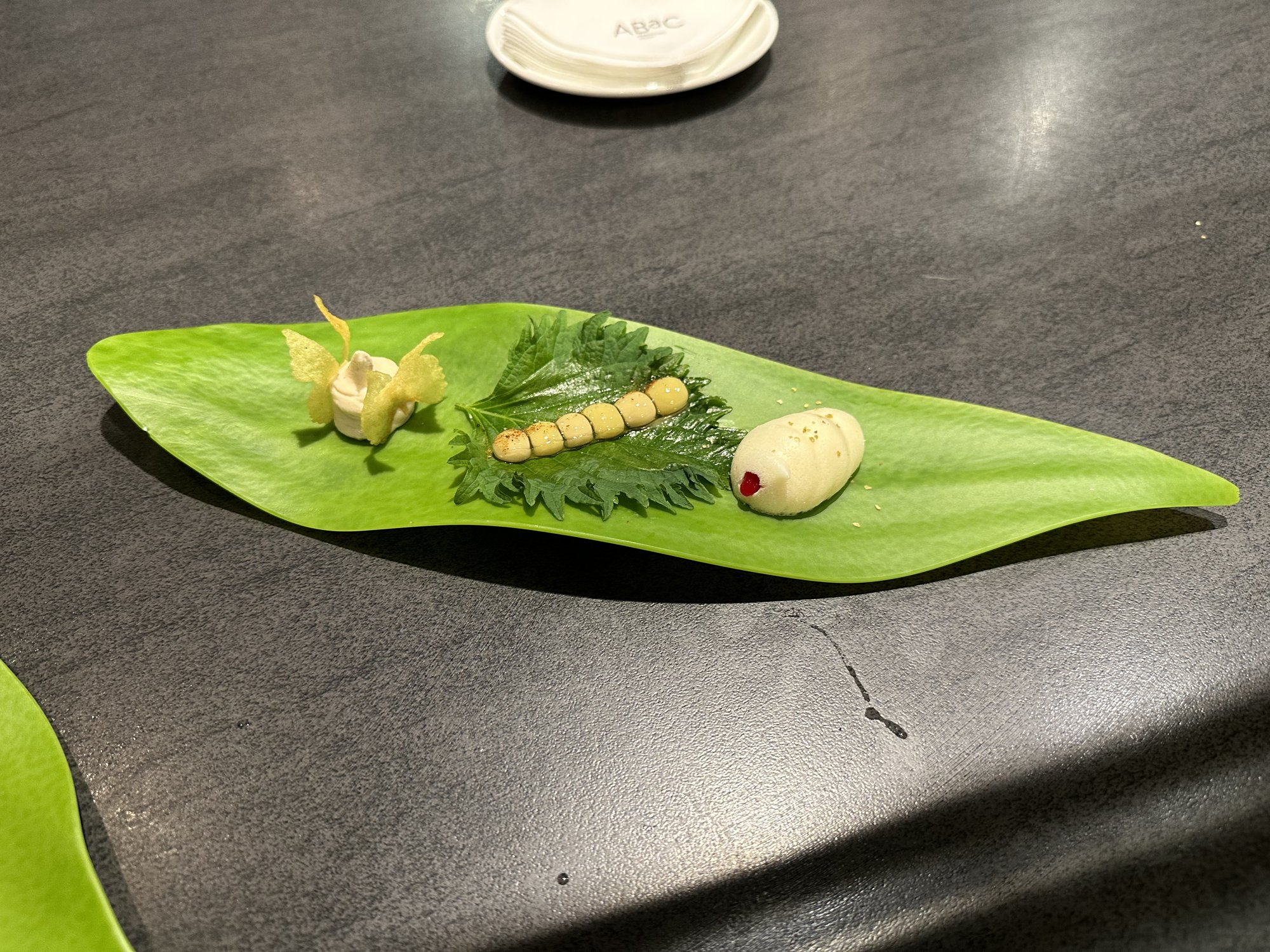 Three small bites arranged along a long green leaf on a dark table