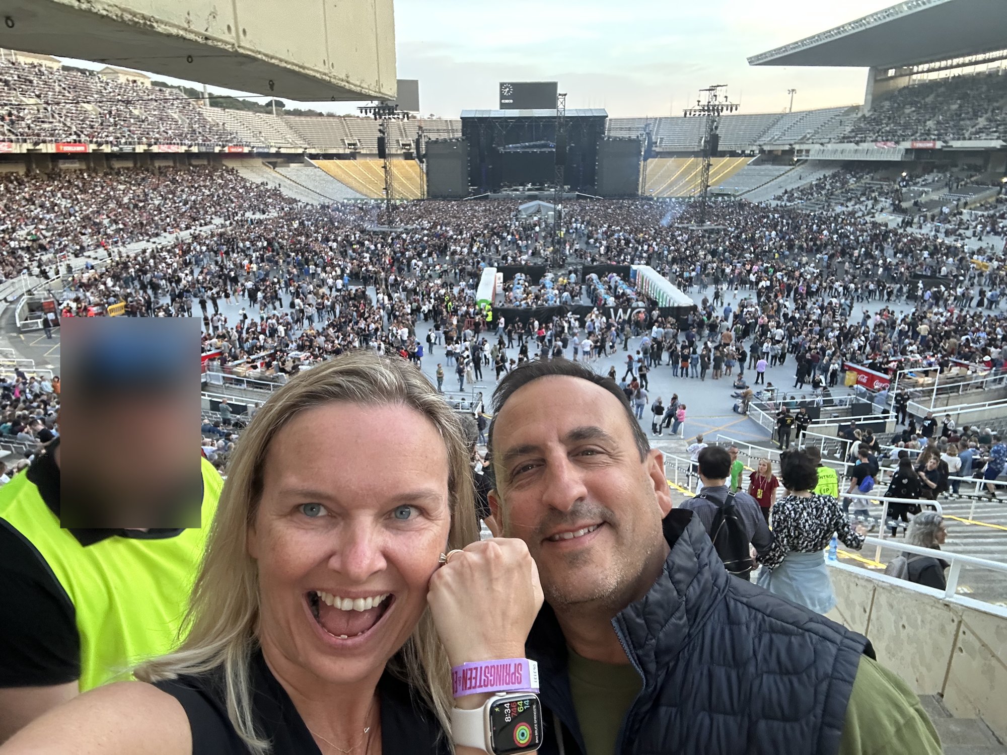 She-Stache and He-Stache taking a selfie in the stands, with the stage and a filling floor behind them