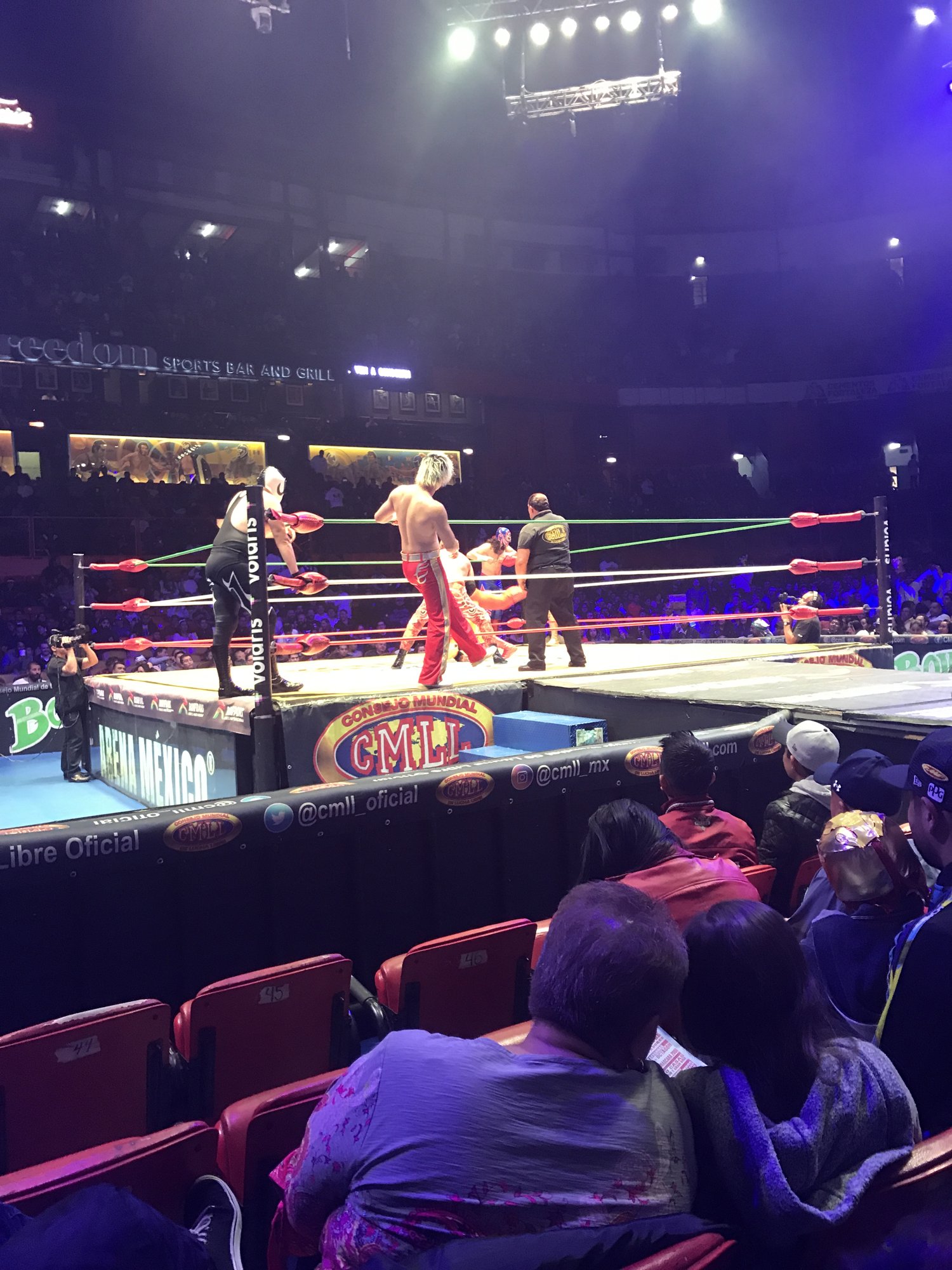 The lit wrestling ring at Arena México seen from the seats, wrestlers mid-match