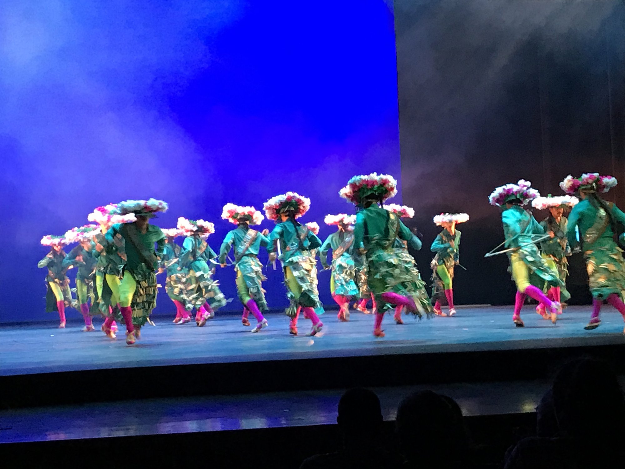 Dancers in green costumes spread across a blue-lit stage