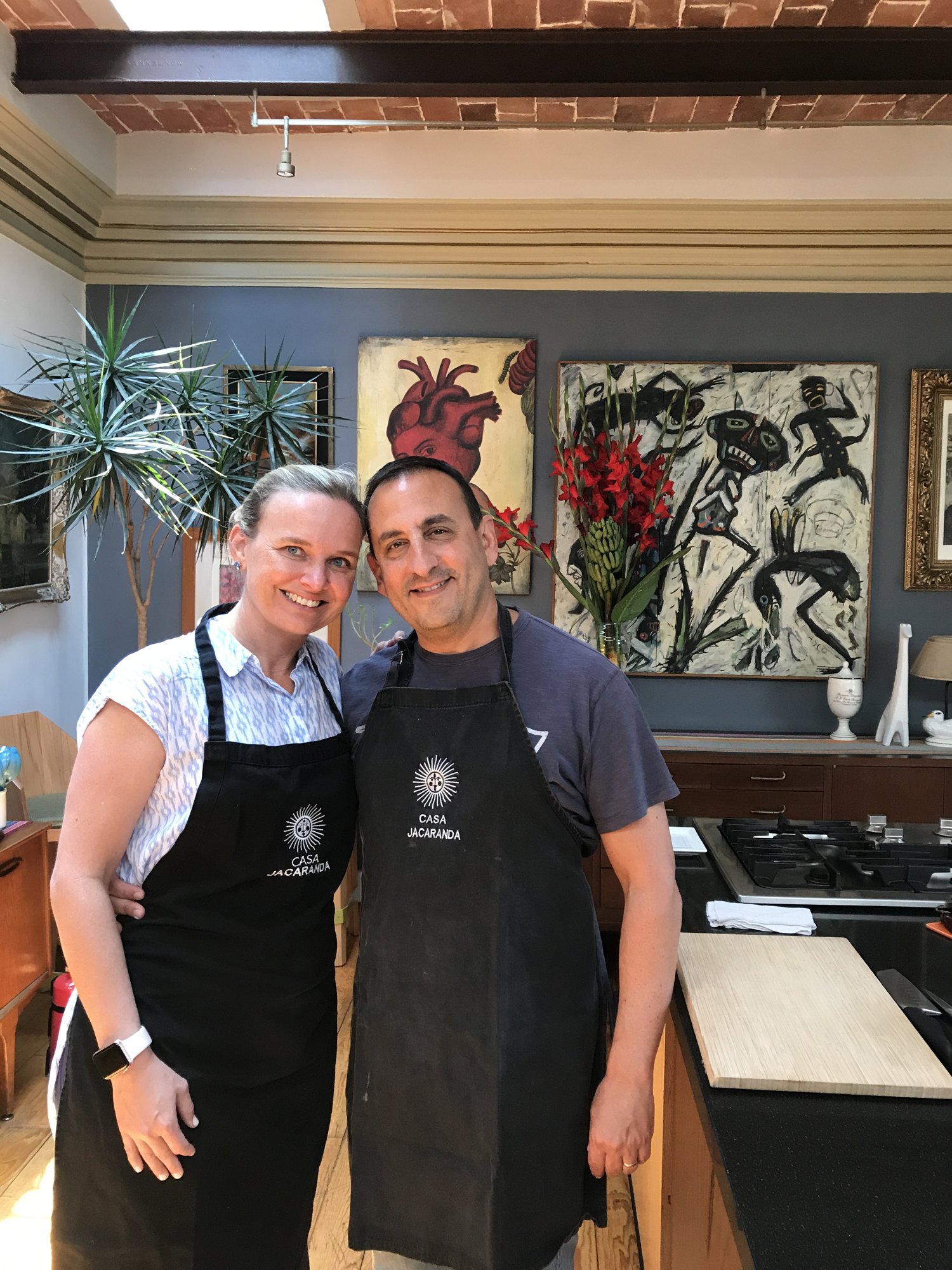 Two people in black aprons in the Casa Jacaranda kitchen, framed art on the wall behind