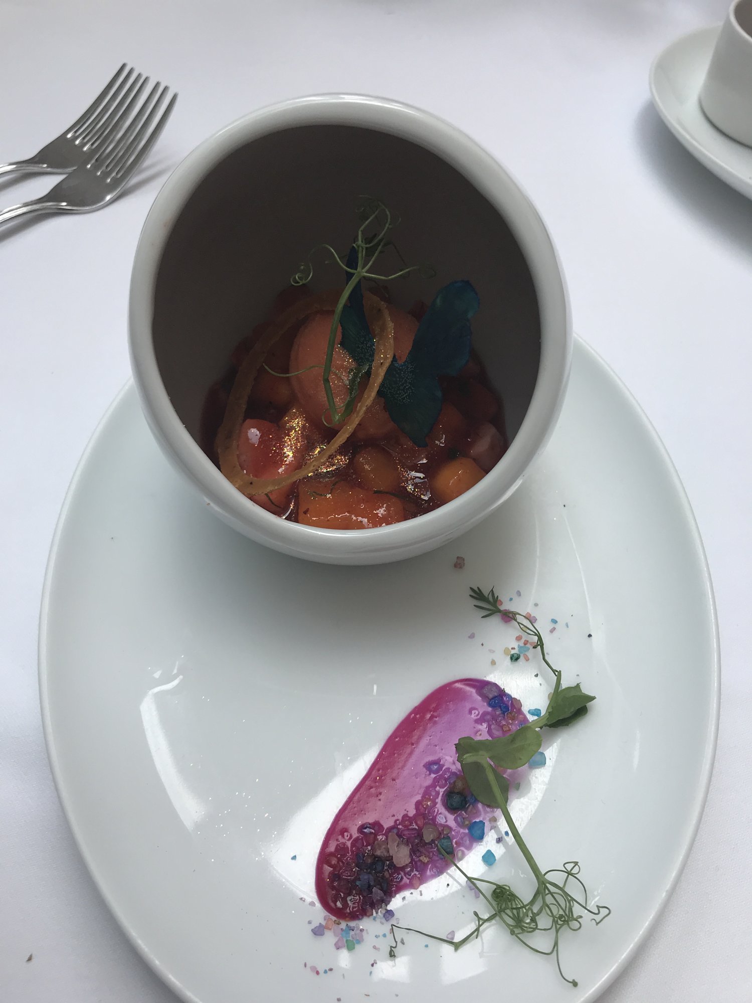 A bowl of stew beside a swipe of beet purée on a white plate