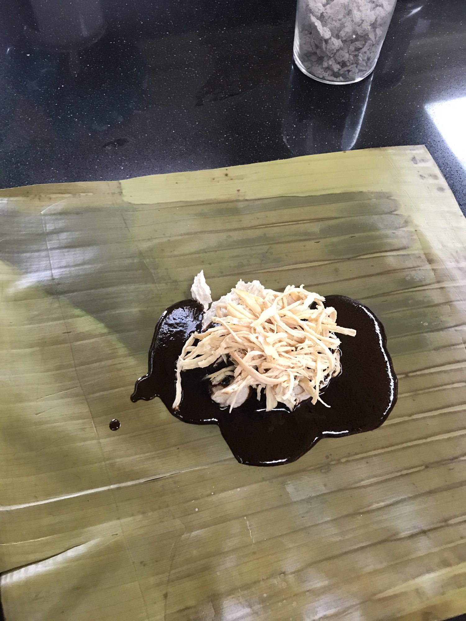 Mole and shredded chicken spooned onto a banana leaf