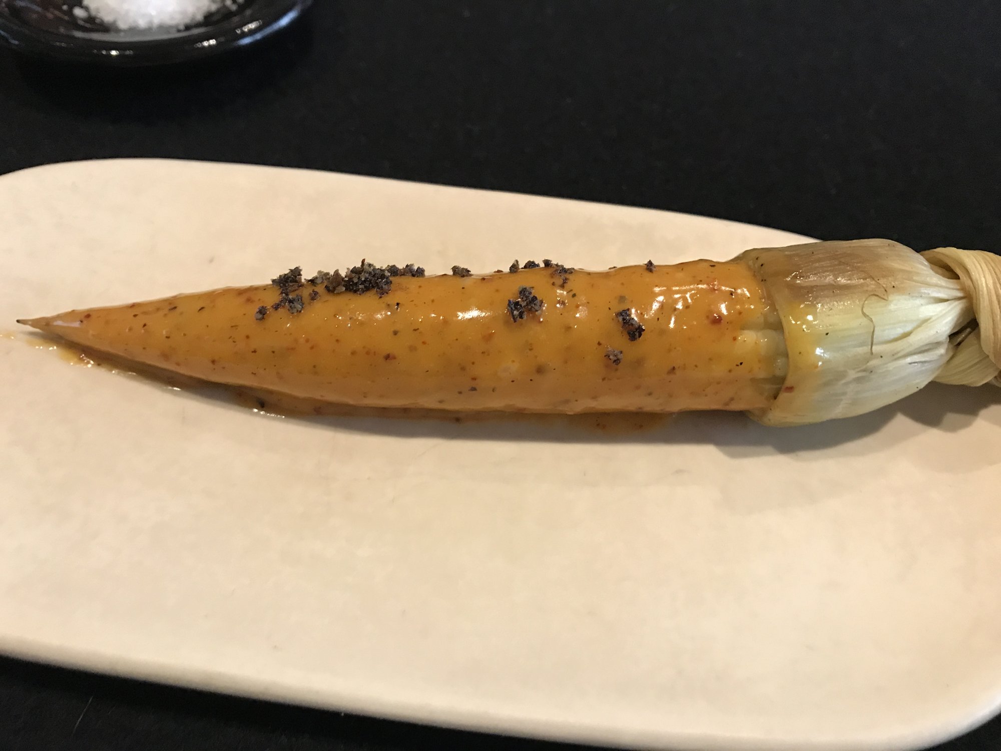A golden corn-husk dish topped with dark seasoning on a white plate at Pujol&rsquo;s bar