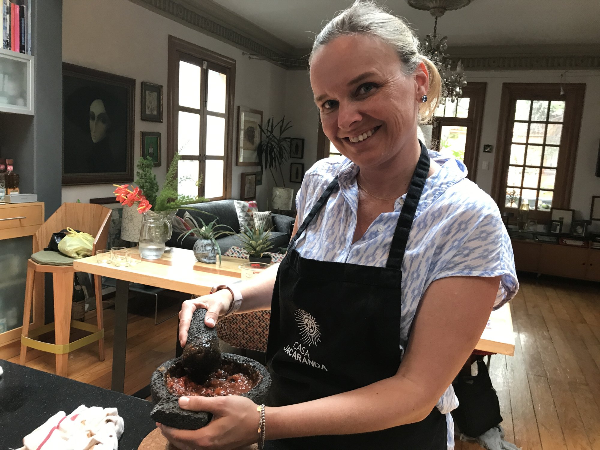 She-Stache in an apron, smiling, grinding salsa in a stone molcajete