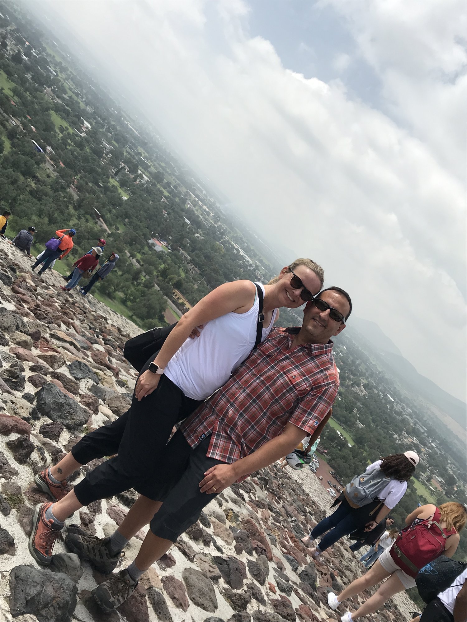 She-Stache and He-Stache leaning into a selfie partway up a steep pyramid staircase, the valley far below