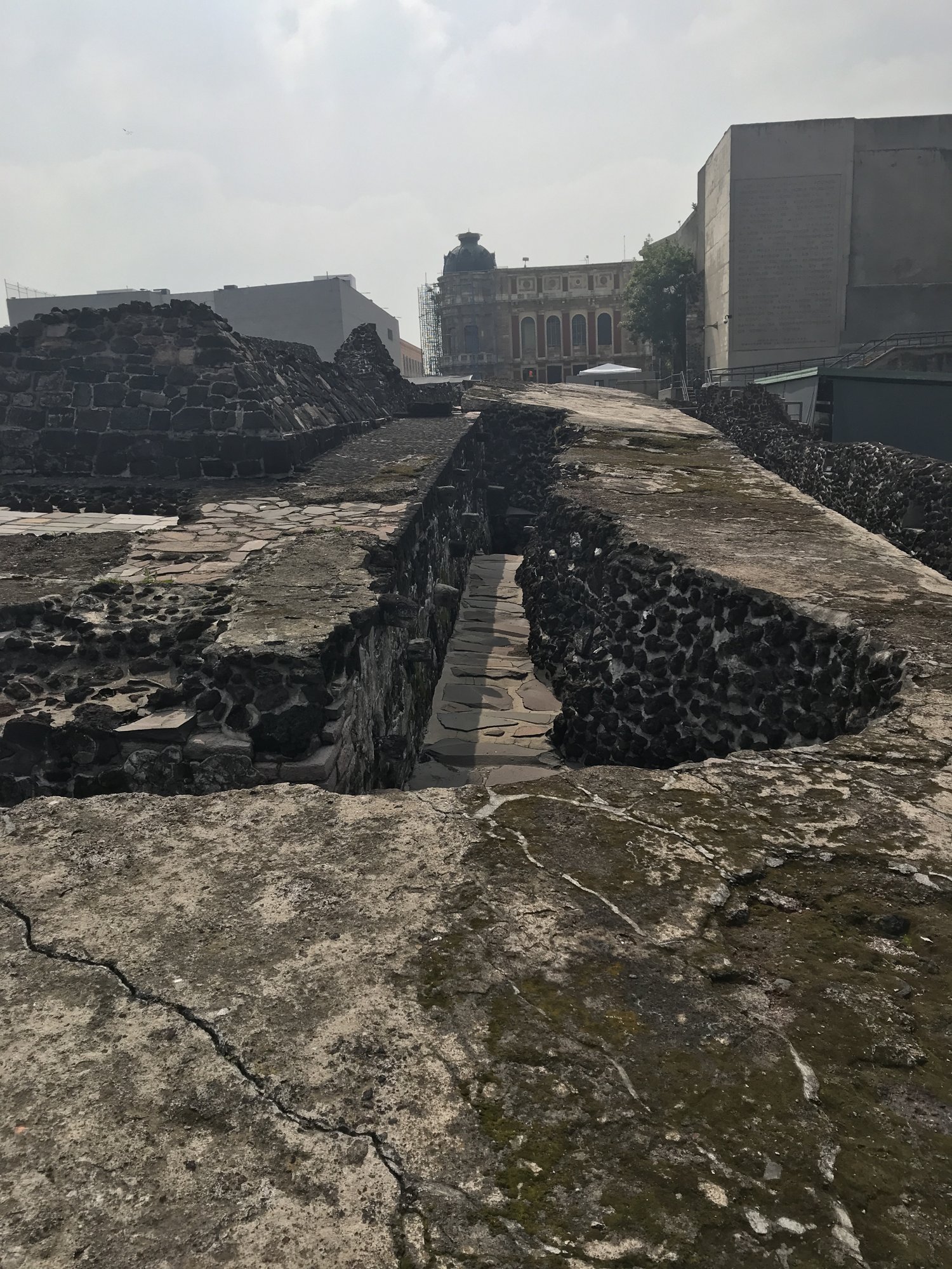 Layers of excavated Aztec temple walls with colonial buildings rising behind them