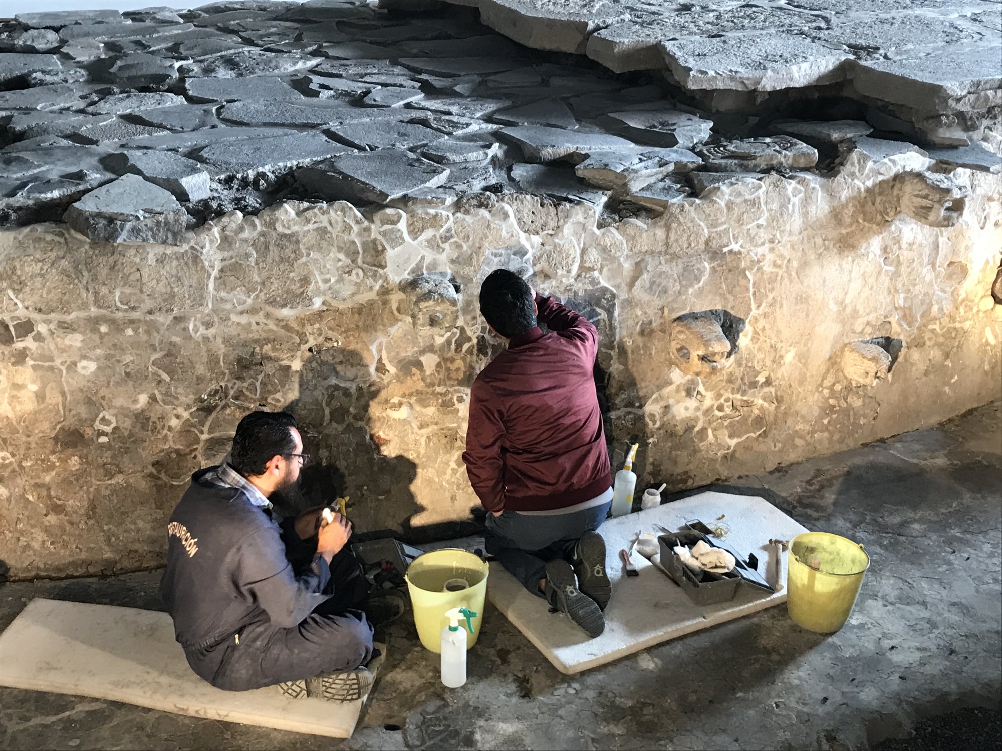 Workers restoring stonework under a protective roof inside the Templo Mayor site