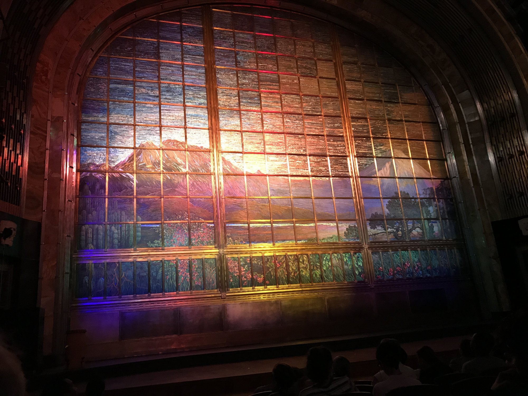 The theater&rsquo;s glass mosaic curtain lit up, a mountain landscape in colored glass