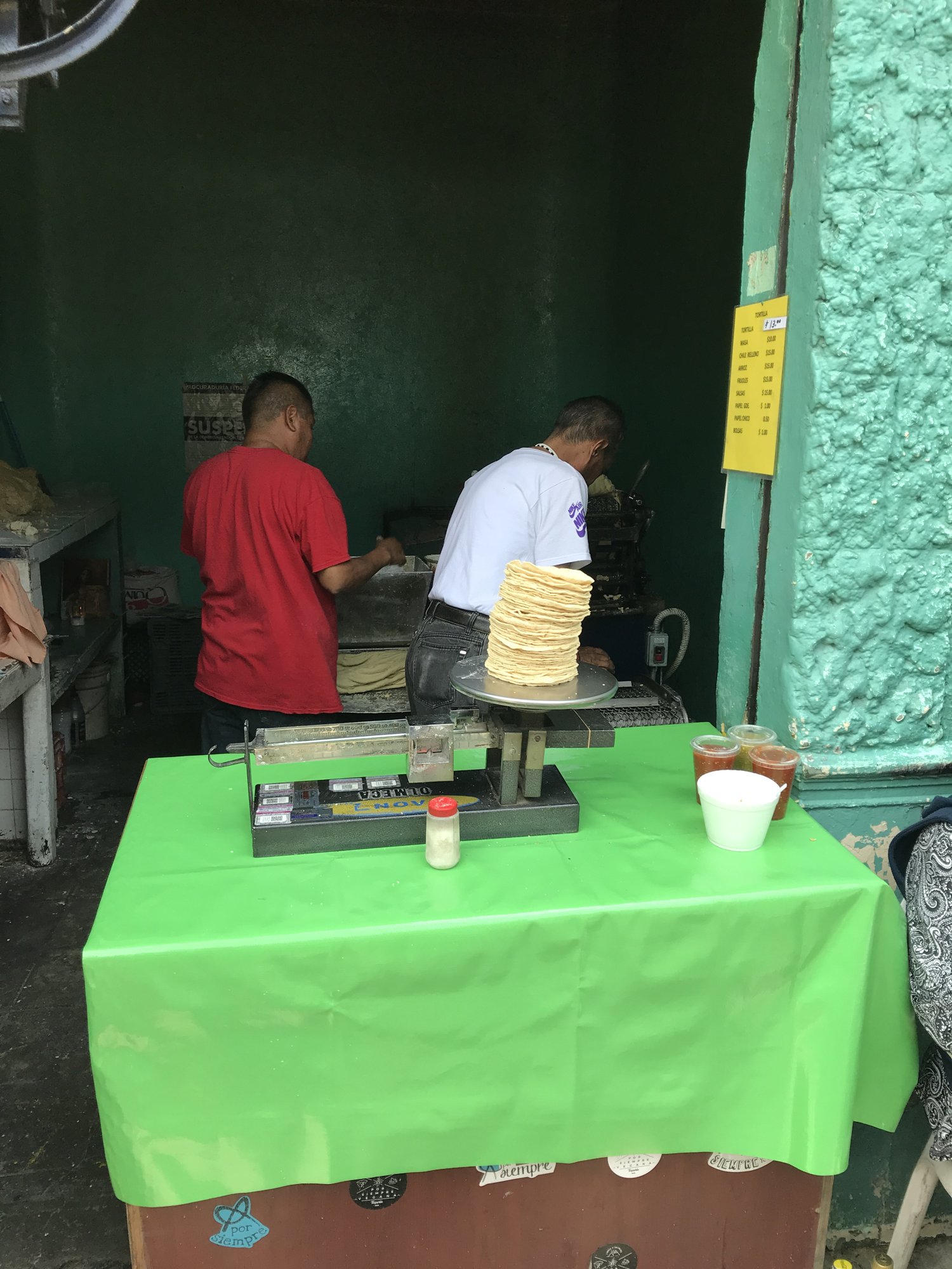 A tortilla stand with a scale and stacks of tortillas on a green table