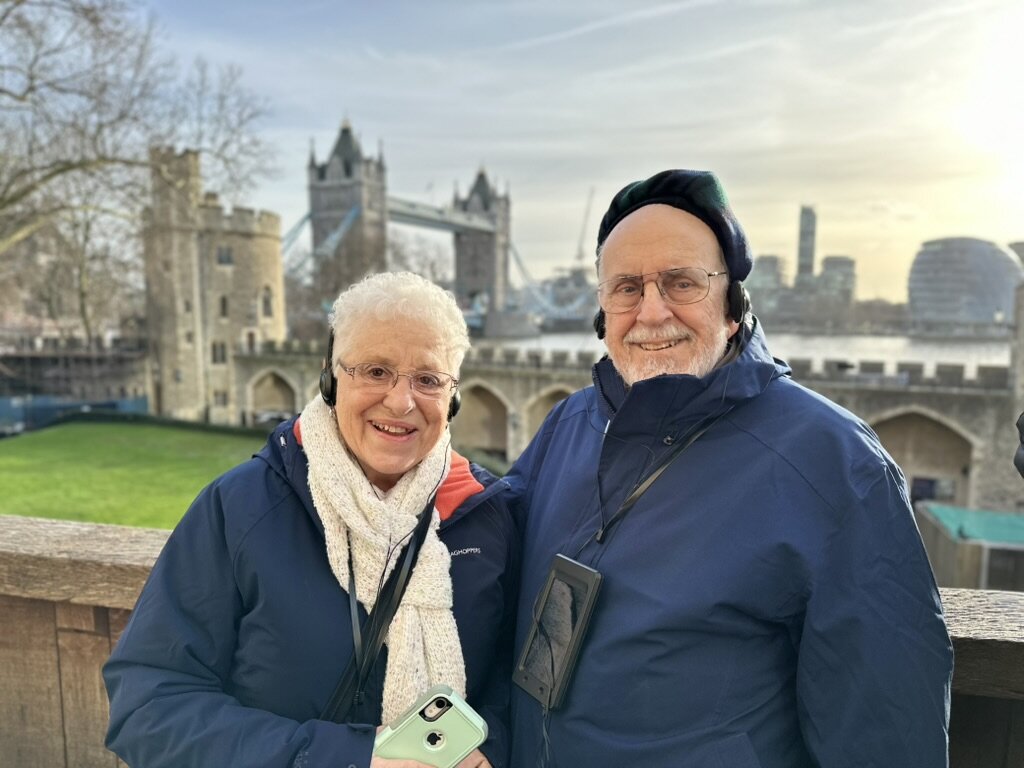 Mom and Dad in audio guide headsets at the Tower of London with Tower Bridge behind them