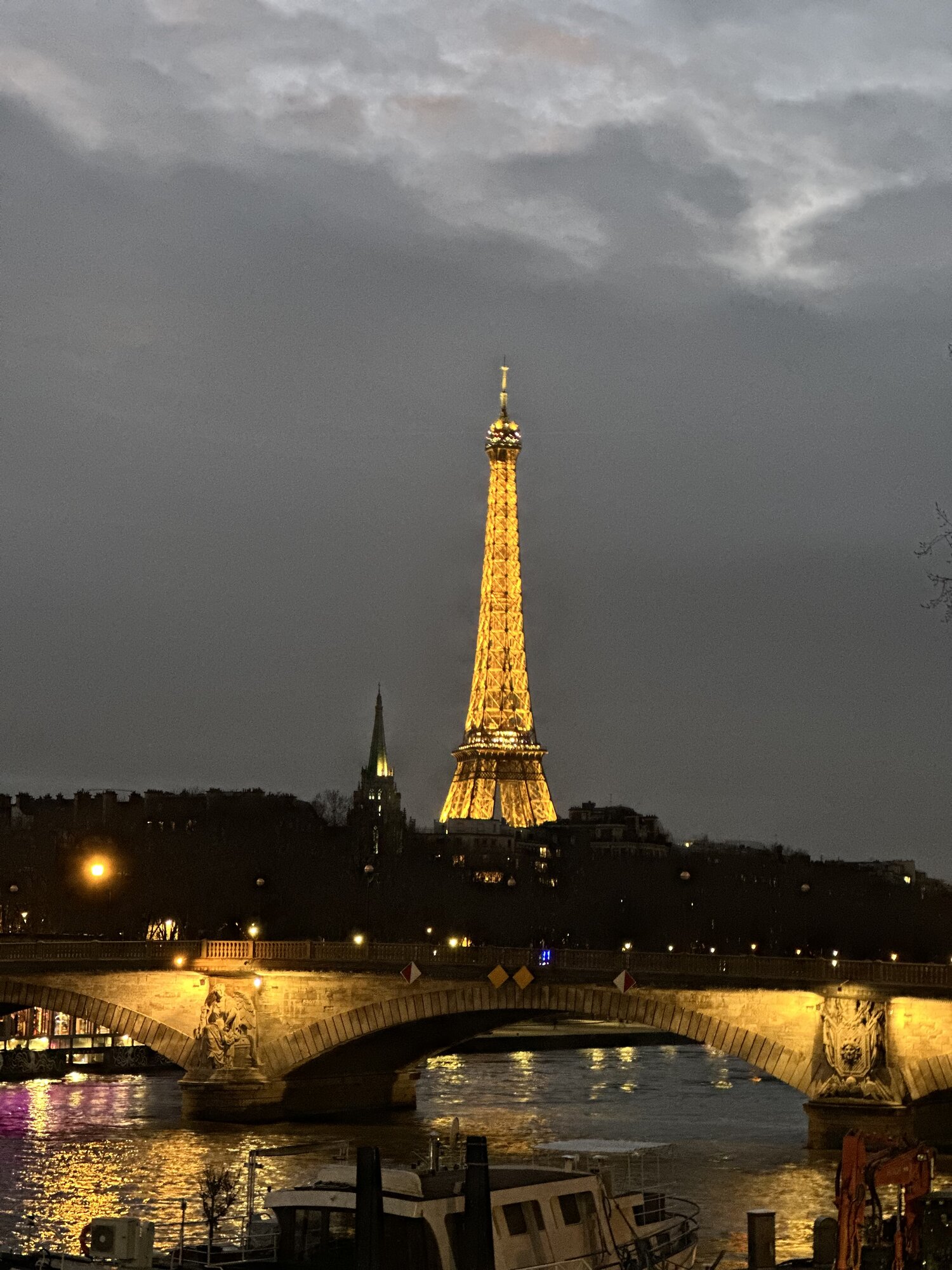 The illuminated Eiffel Tower at night, seen from a bridge over the Seine