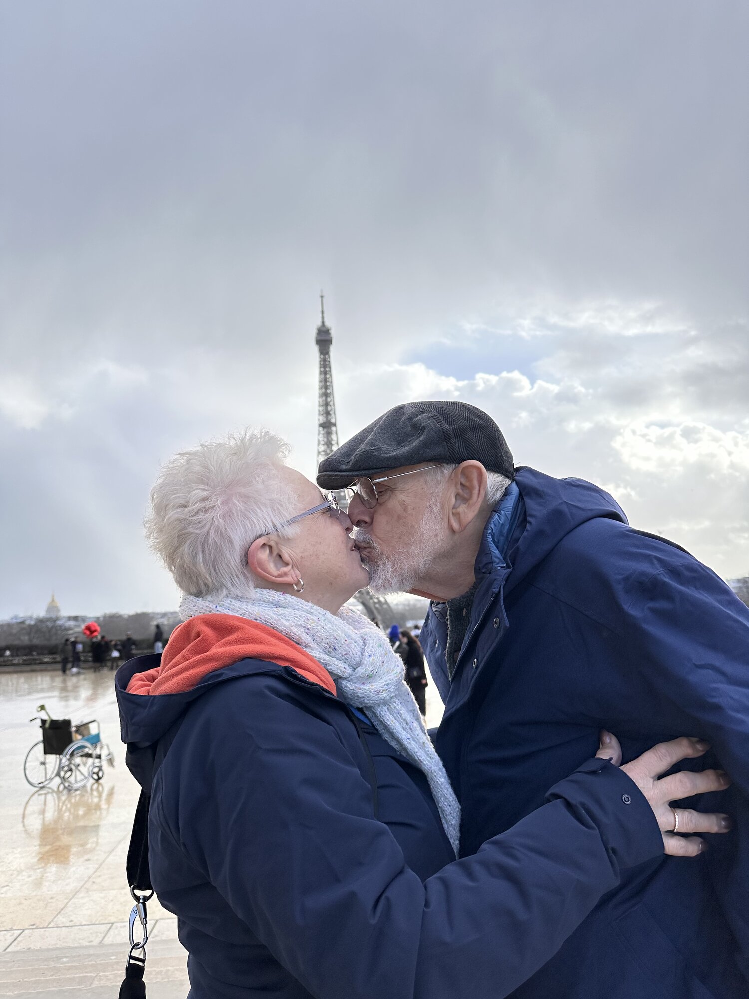 Mom and Dad kissing in the rain near the Eiffel Tower, Dad's empty wheelchair beside them