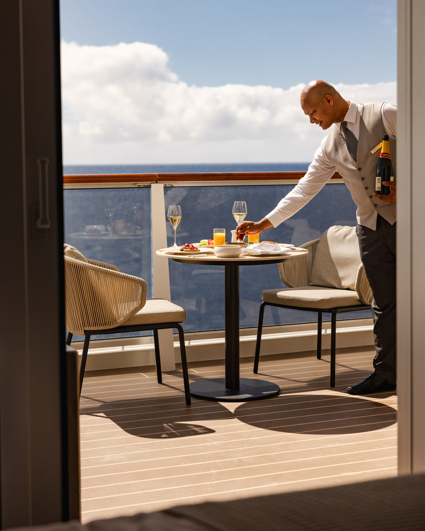 Explora media kit photo of a crew member setting breakfast on a stateroom balcony table overlooking the sea