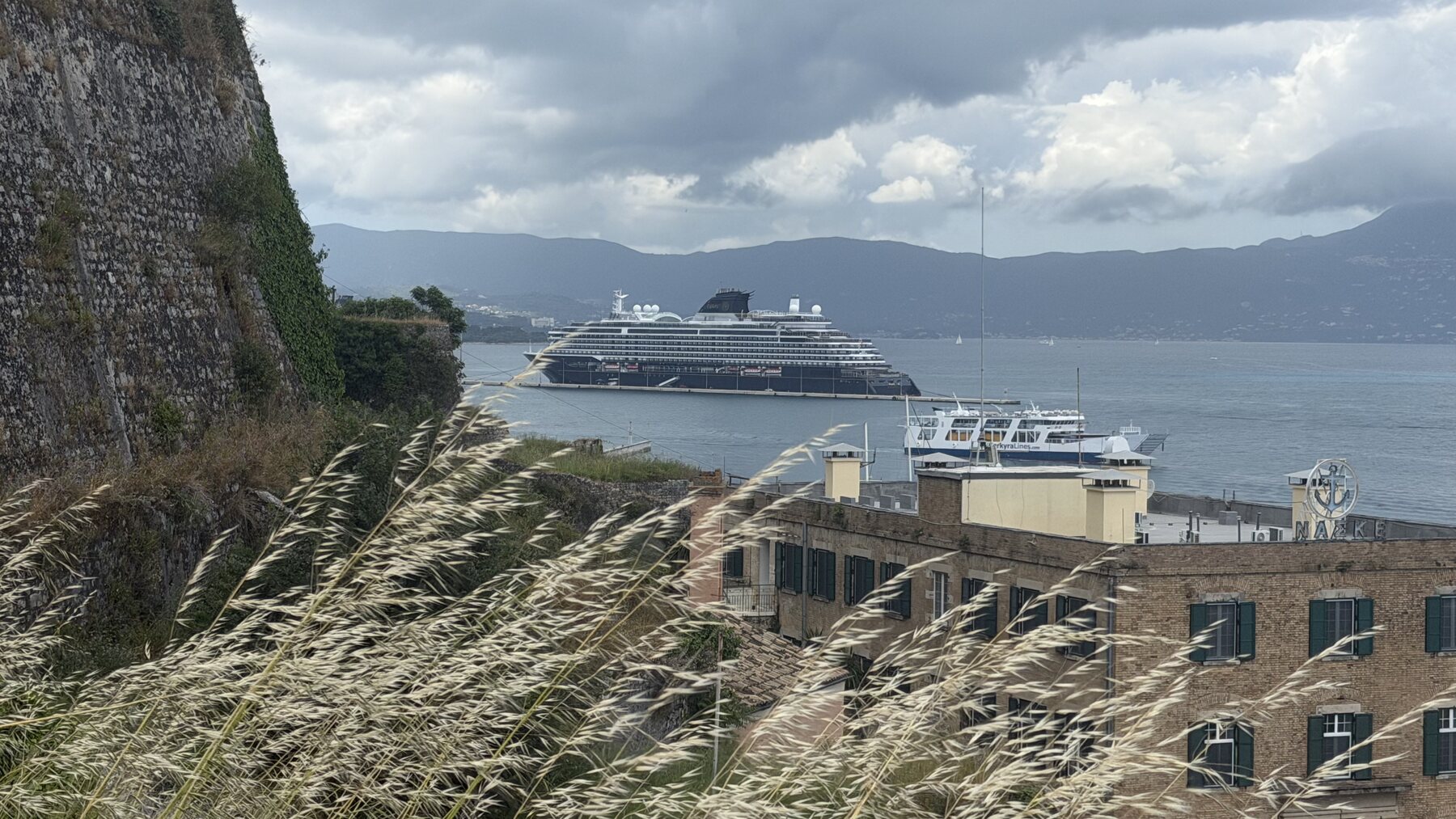 Explora II docked in the Corfu harbor, seen from the fortress walls through tall grass