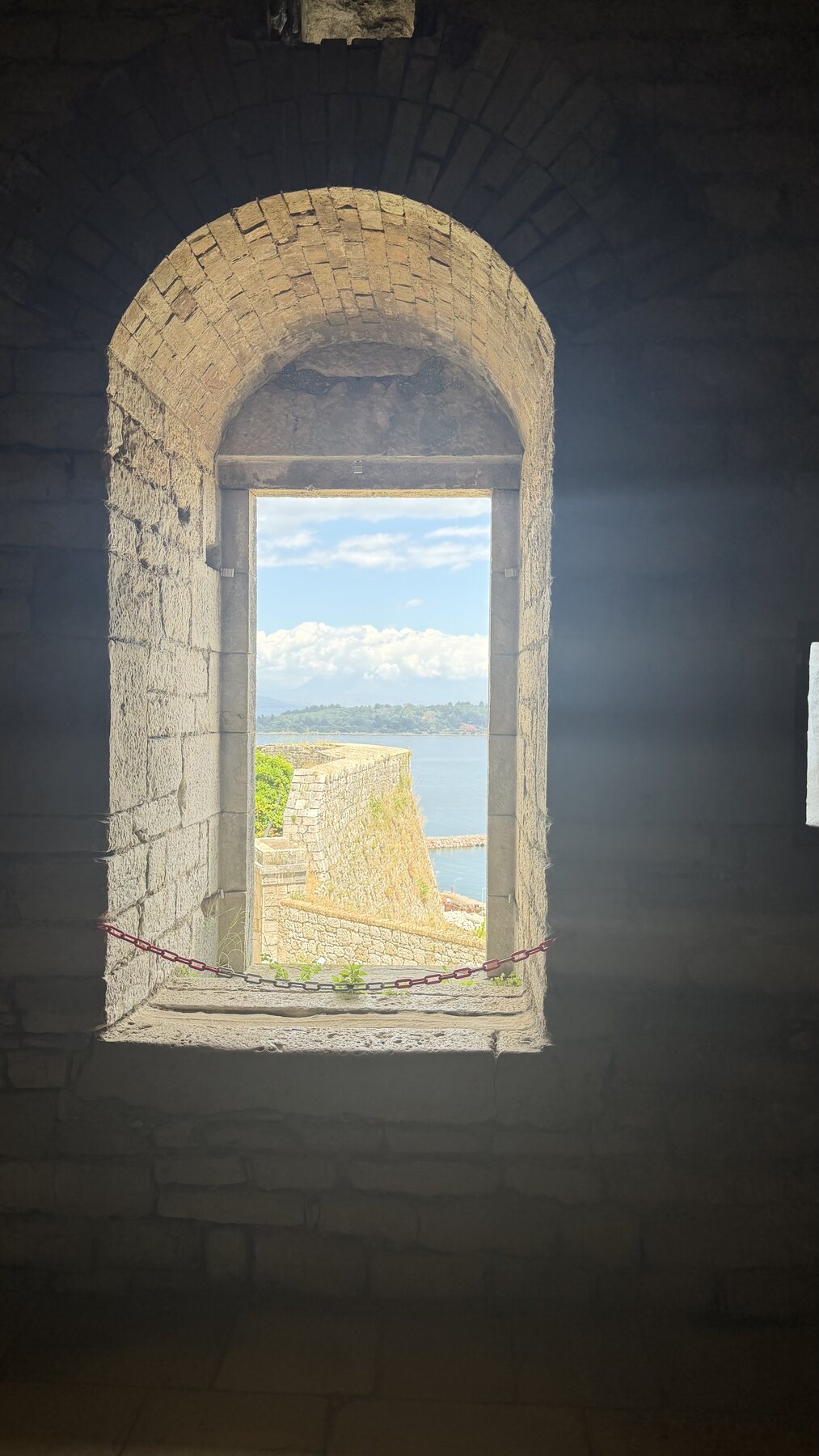 A narrow stone window inside the fortress framing a slice of sea and rampart
