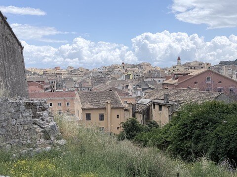 Terracotta rooftops and pastel Venetian buildings of Corfu Town under puffy white clouds