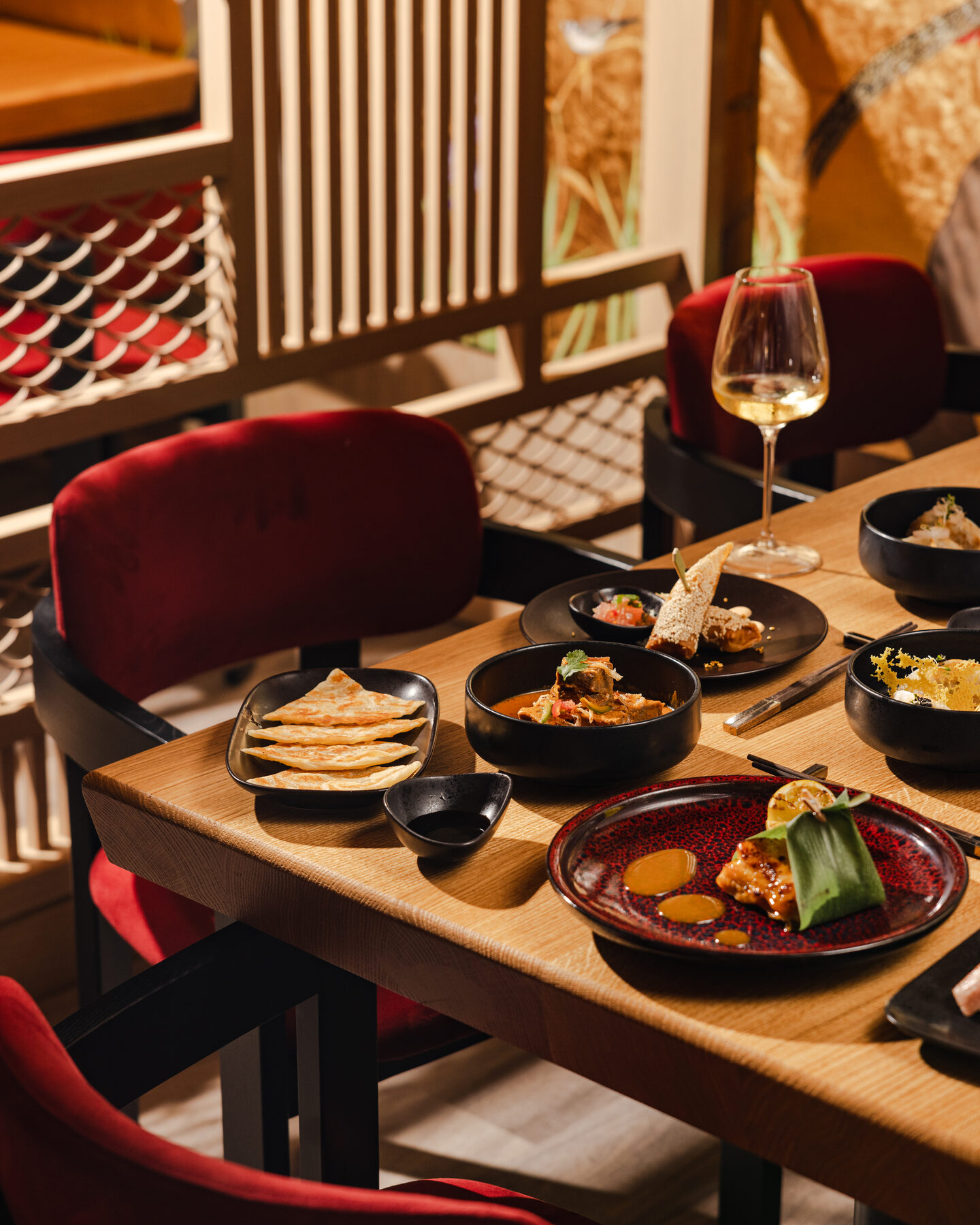 Explora media kit photo of a dinner table set with small plates, dumplings, and a glass of white wine beside red velvet chairs