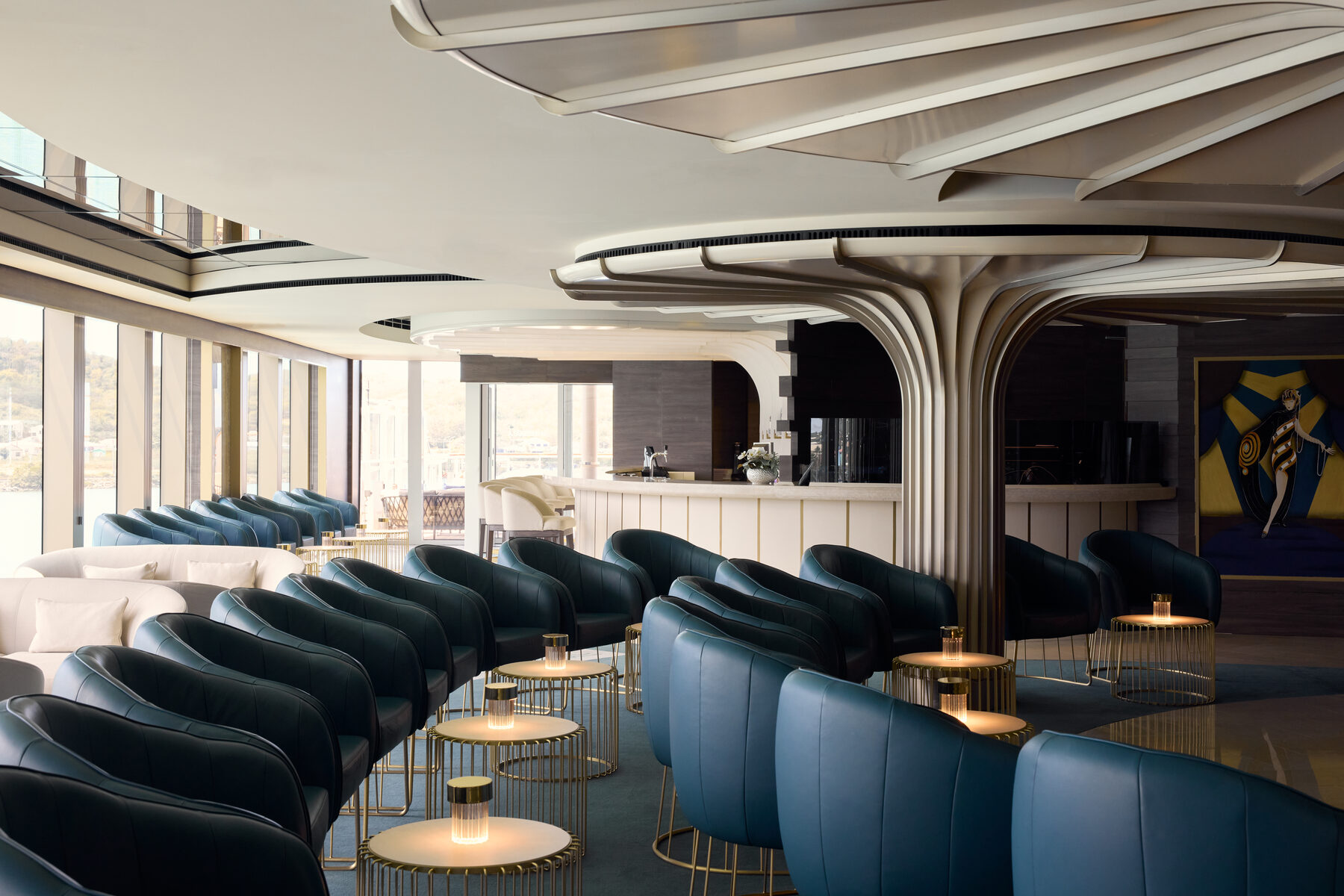 Explora media kit photo of the Explora Lounge, rows of blue leather armchairs and lamplit side tables beside floor-to-ceiling windows