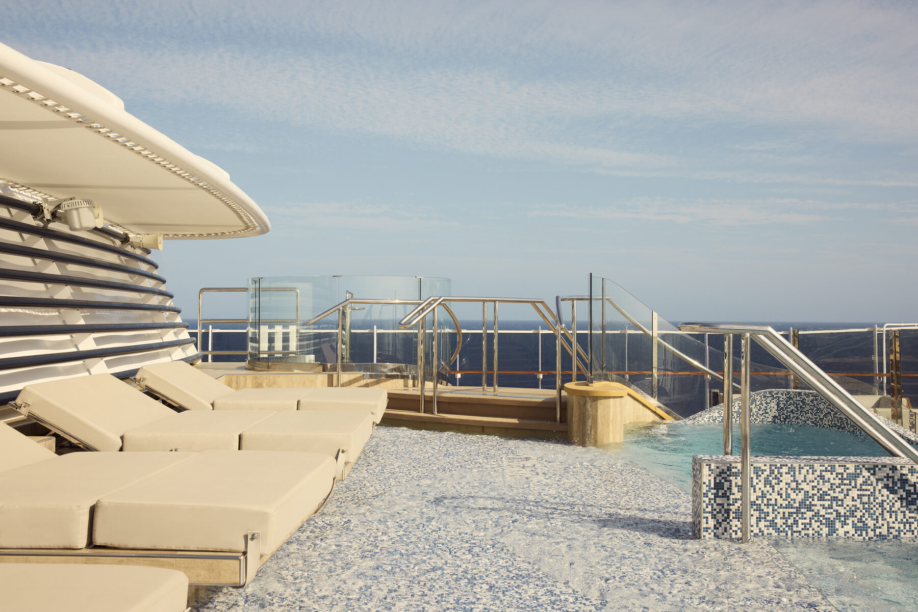 Explora media kit photo of a shallow mosaic-tiled pool and cream loungers on the top deck under a clear sky