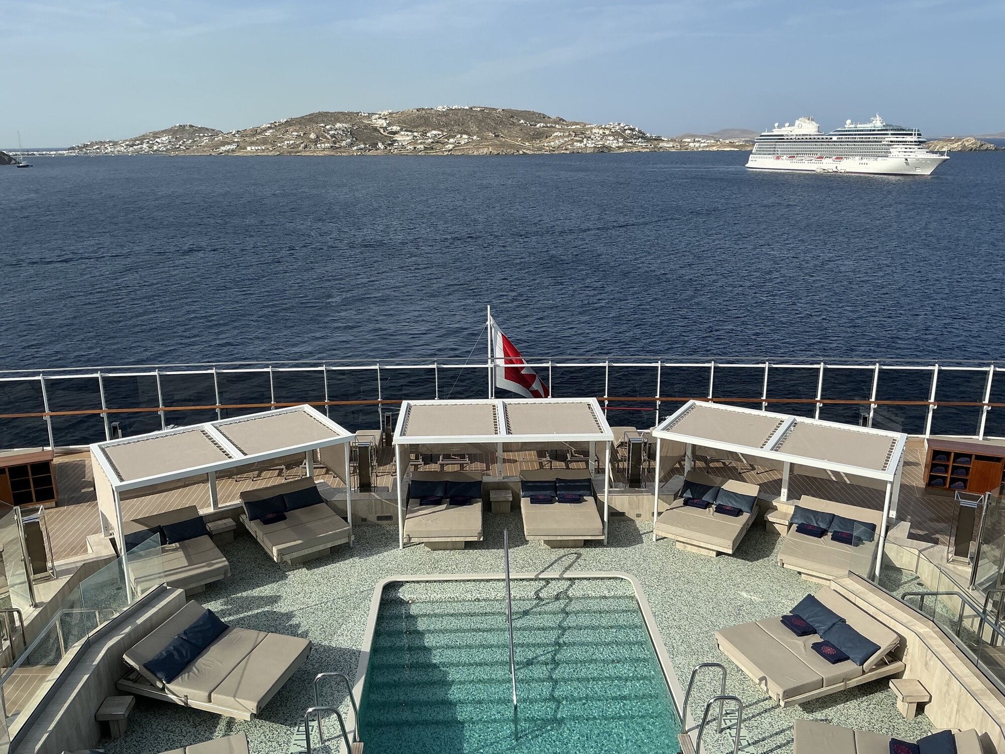 Explora II&rsquo;s empty aft pool and shaded loungers, anchored off Mykonos with another cruise ship across the bay