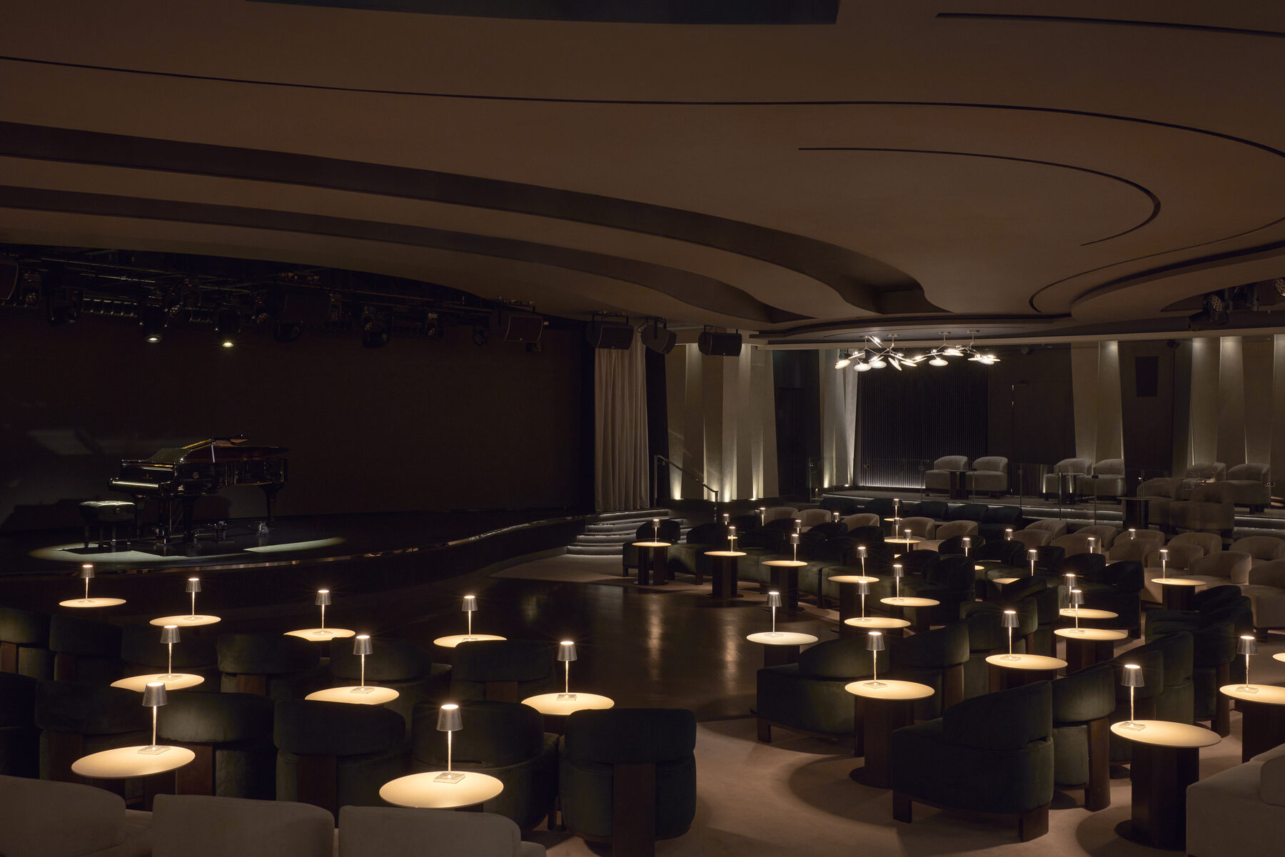 Explora media kit photo of the Journeys Lounge, a grand piano on stage, a dance floor, and lamplit tables among velvet armchairs