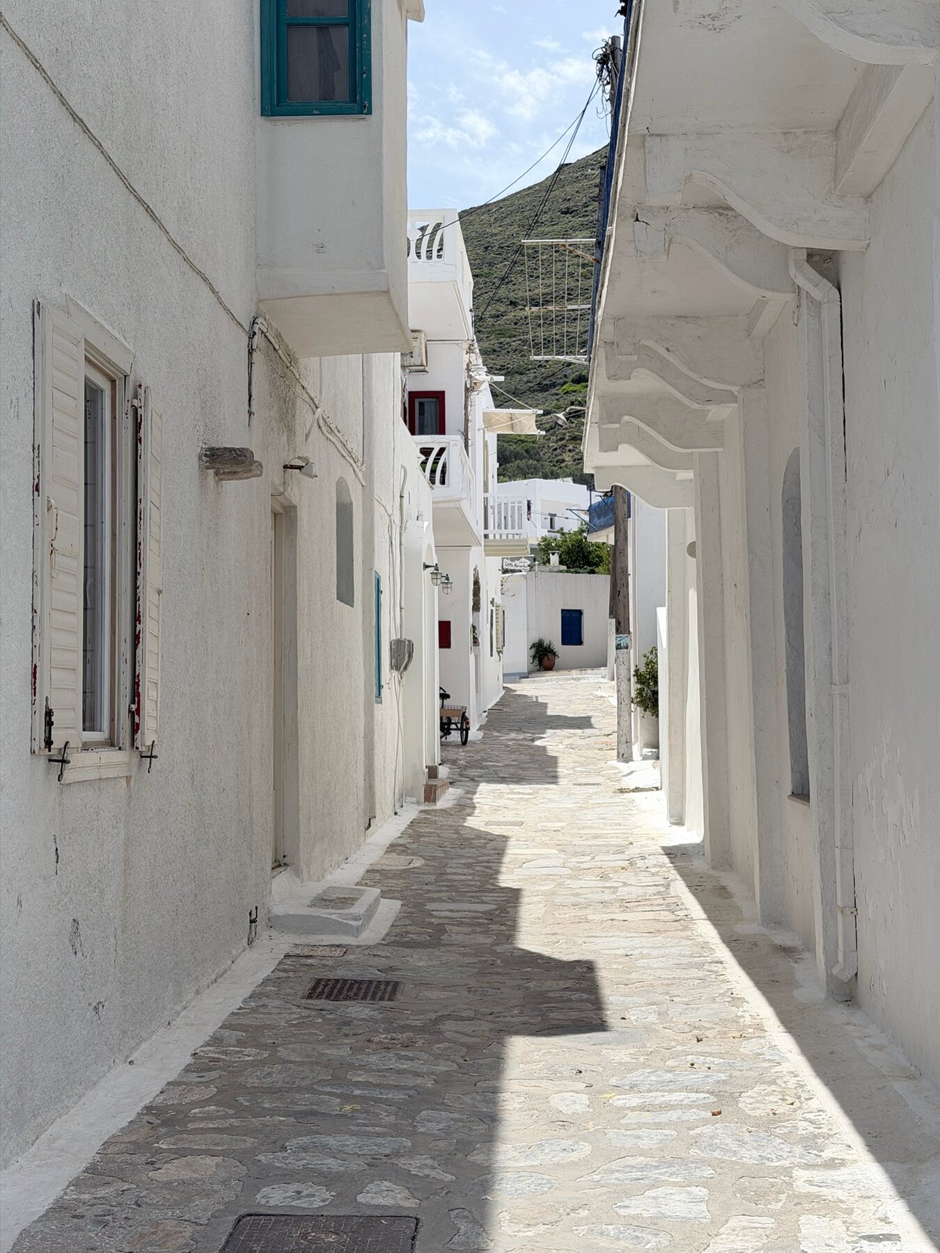 A narrow whitewashed lane with stone paving and teal shutters in Katapola