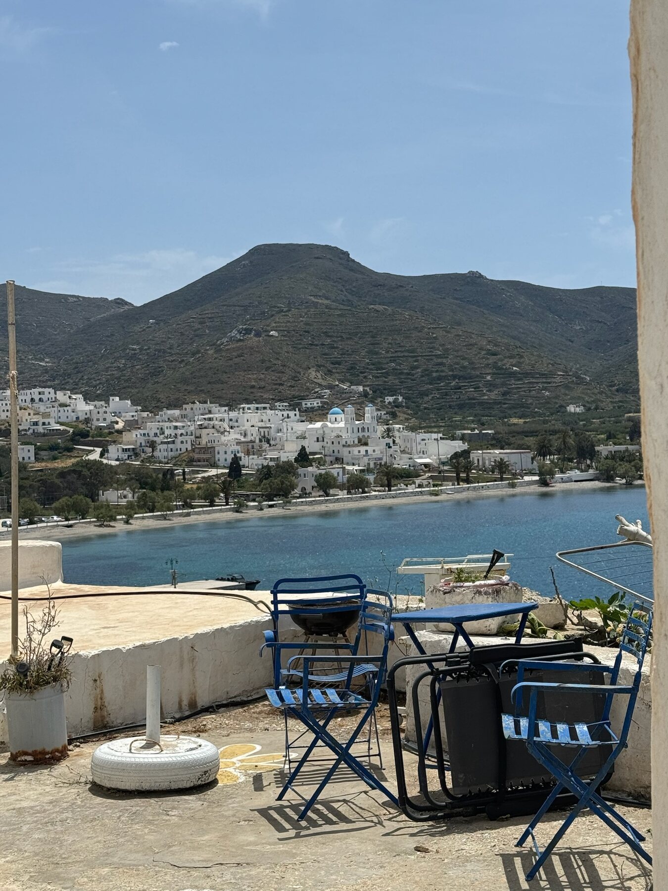 View across the Katapola bay to whitewashed houses and a blue-domed church beneath green terraced hills