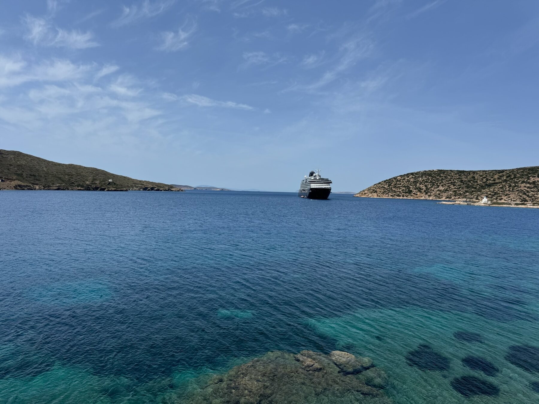 Explora II anchored alone in the turquoise bay outside Katapola, a small white chapel on the point