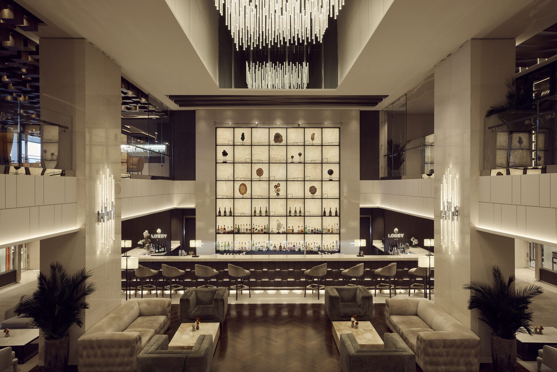 Explora media kit photo of the double-height Lobby Bar with a glass chandelier, a backlit bar wall, and lounge seating