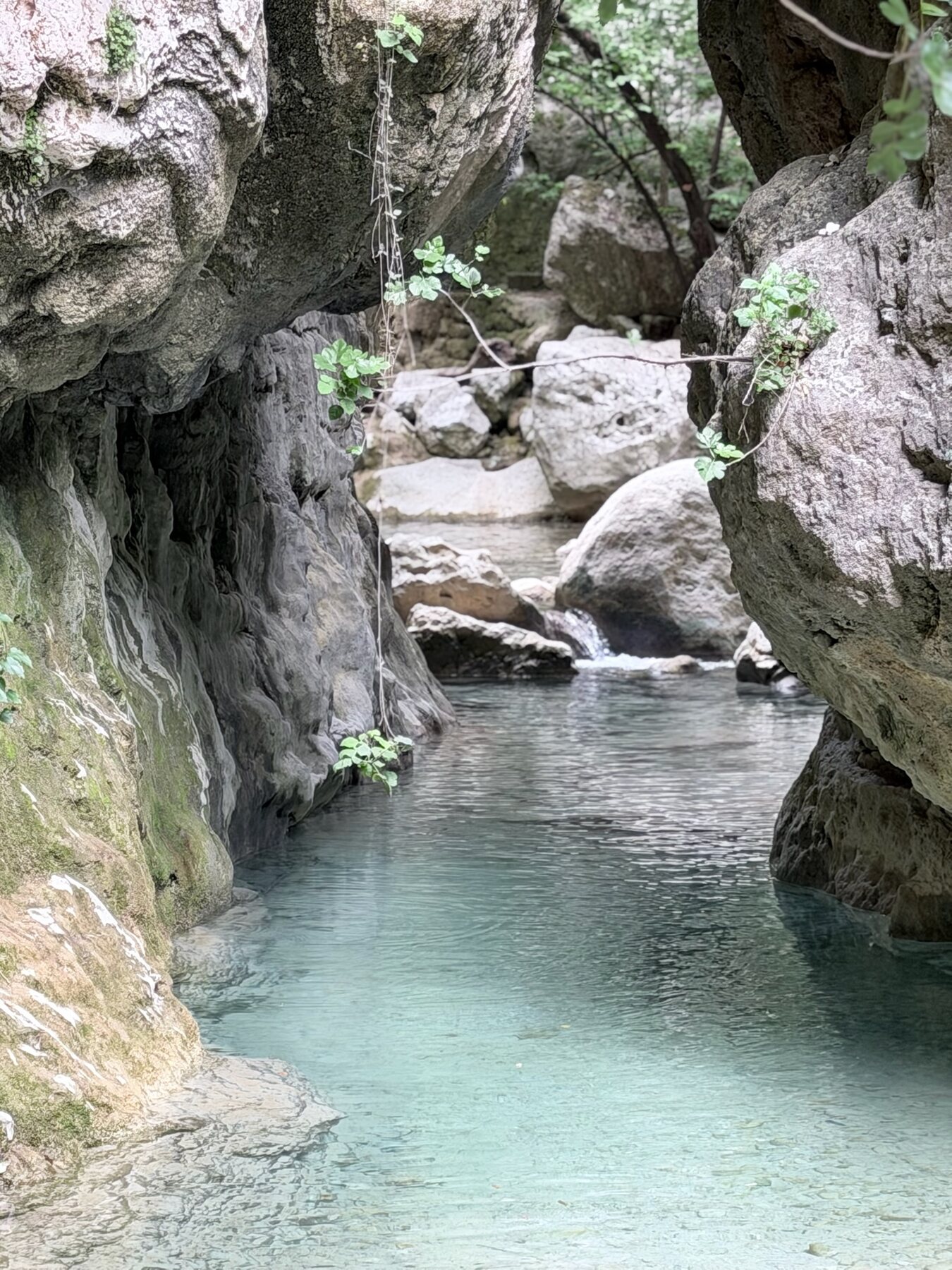 Clear turquoise water winding between huge boulders in the narrow gorge on the hike to the Nydri waterfall