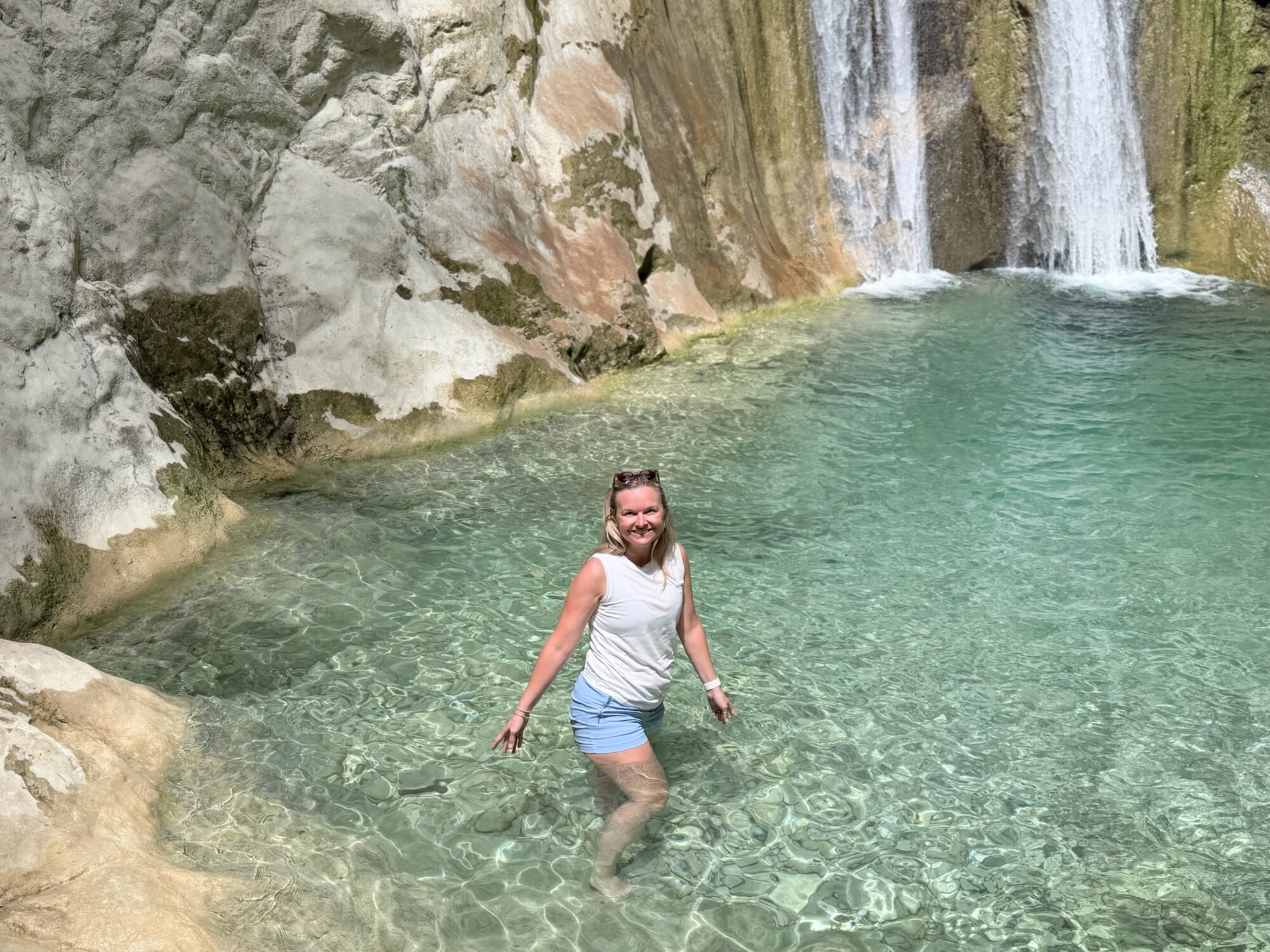 She-Stache smiling, knee-deep in the clear turquoise pool at the foot of the Nydri waterfall