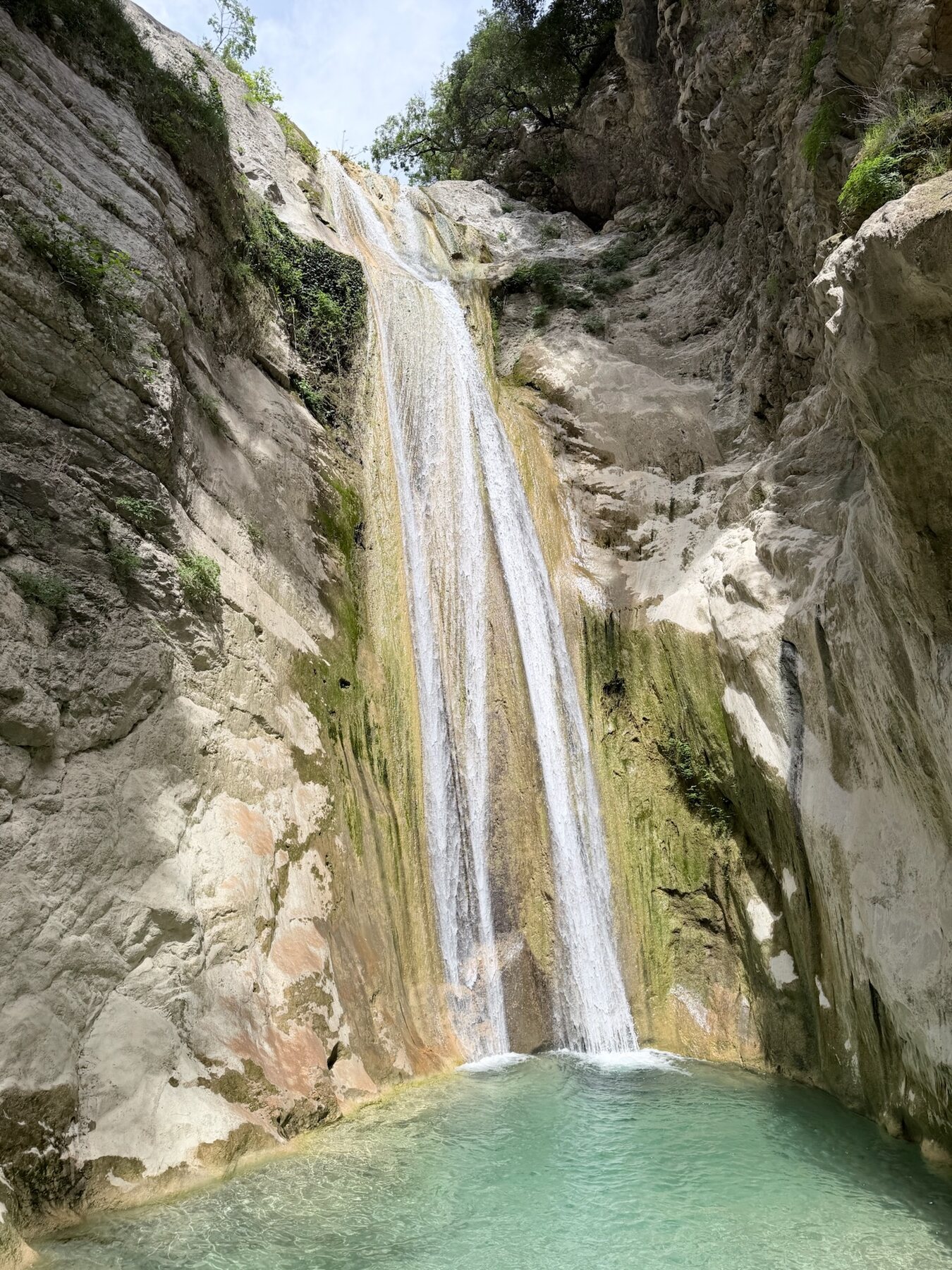 The Nydri waterfall pouring down a tall pale rock face into a green-blue pool