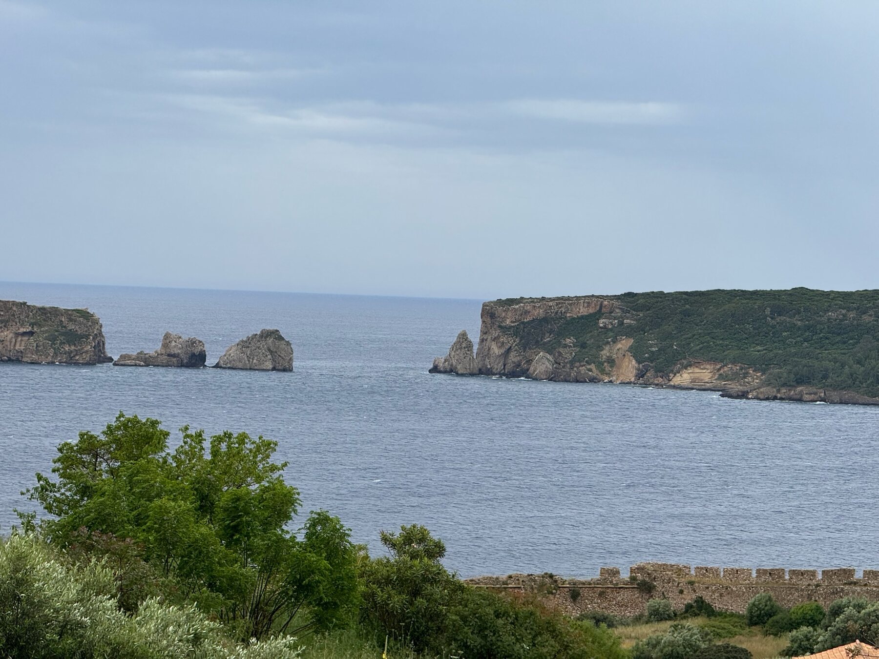 Rock stacks and cliffs at the mouth of Navarino Bay under grey skies, the fortress wall in the foreground