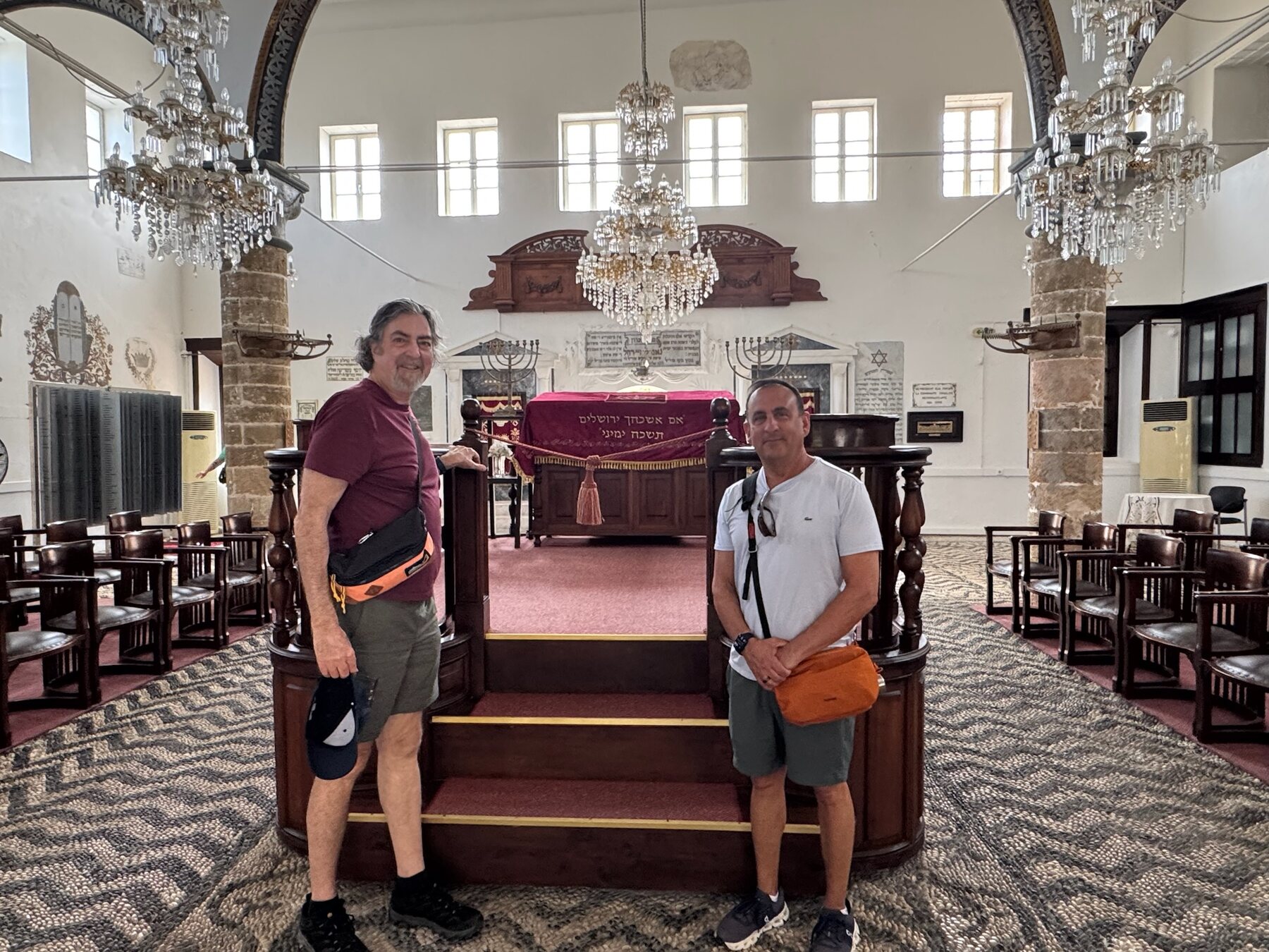 He-Stache and a foodie friend inside Kahal Shalom Synagogue, crystal chandeliers above a pebble-mosaic floor