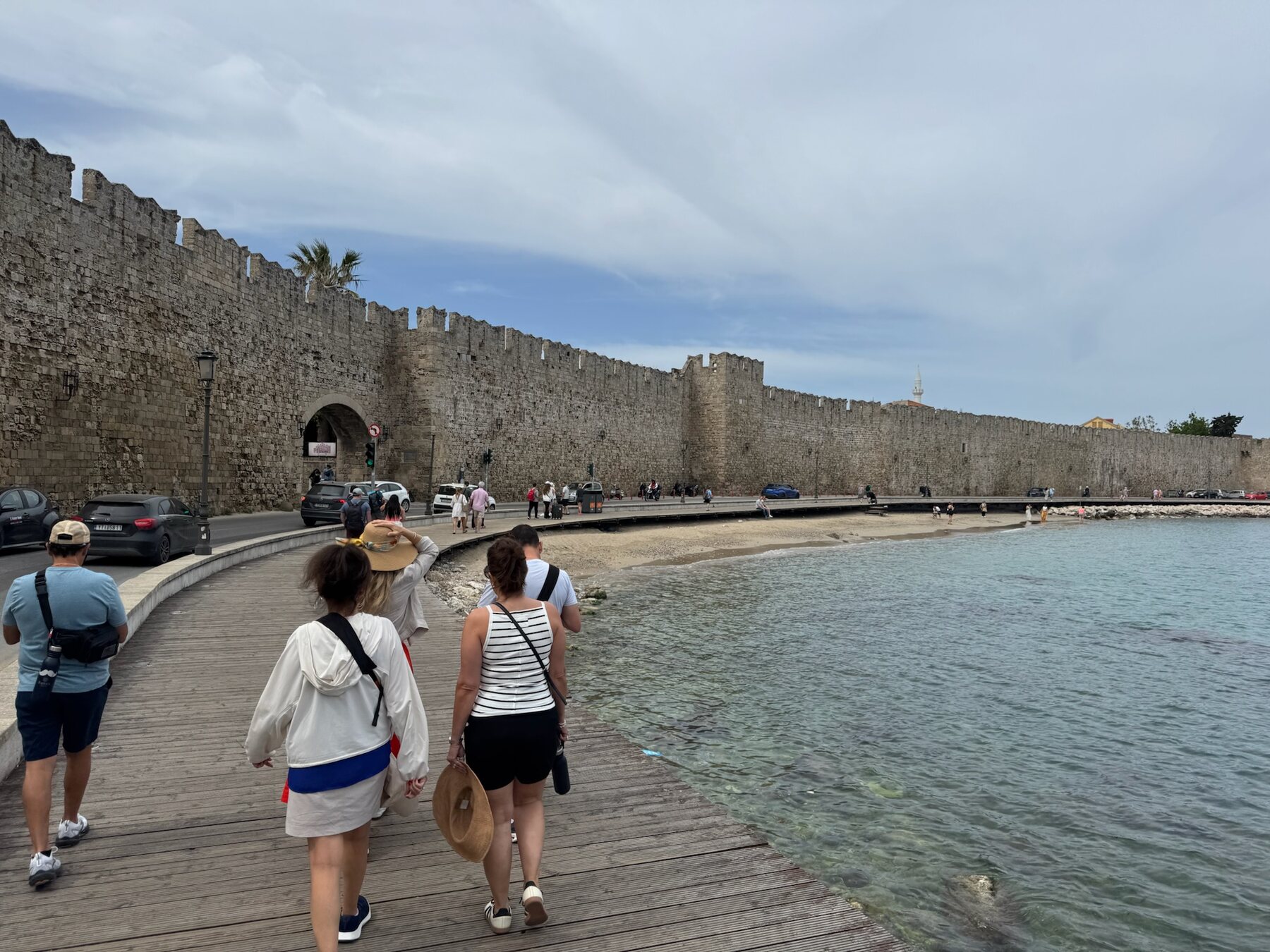 The foodie friends walking a seaside boardwalk beneath the massive crenellated medieval walls of Rhodes