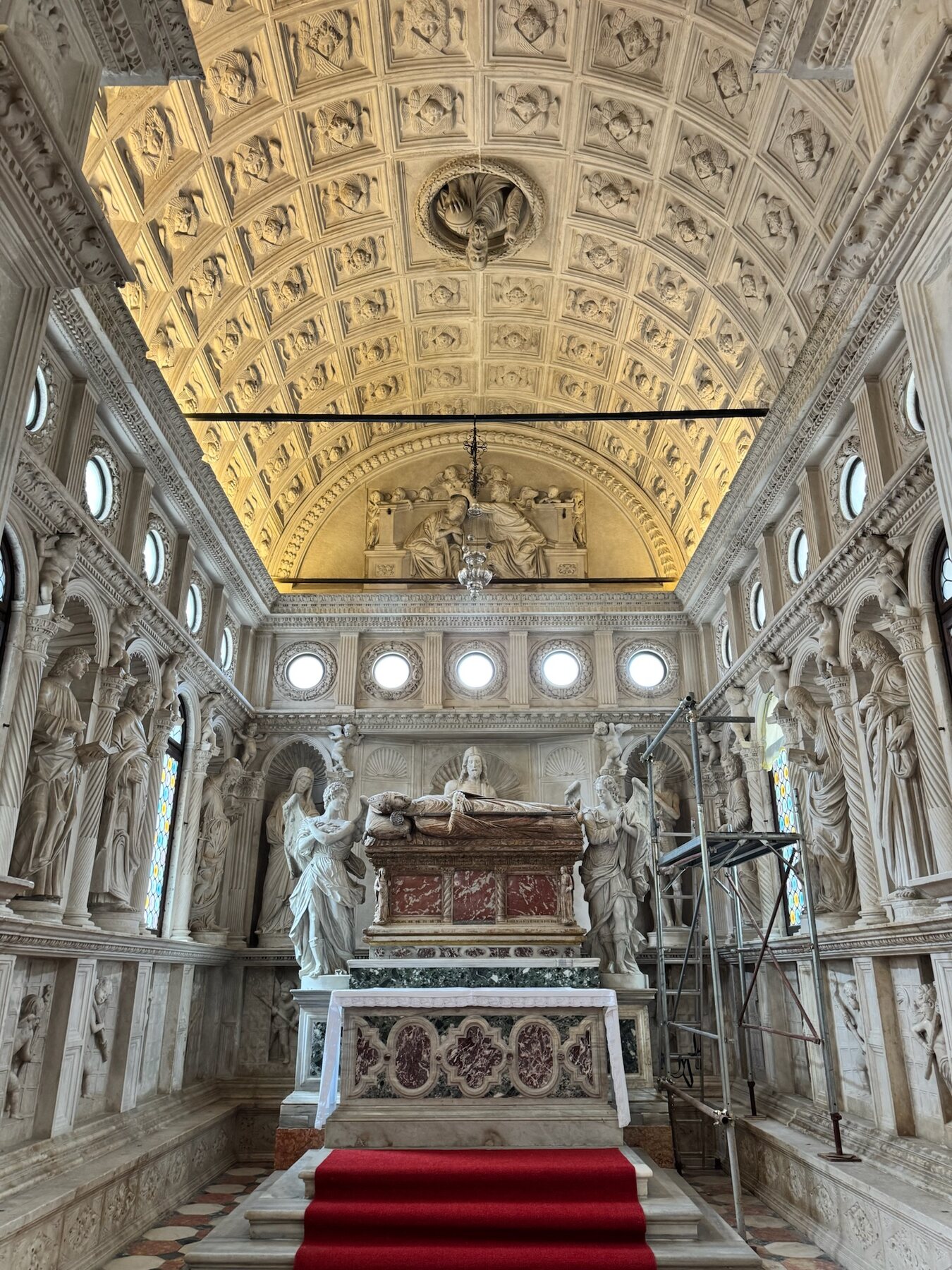 The white marble Renaissance chapel inside Trogir cathedral, a coffered ceiling of carved angels above a tomb and red-carpeted altar