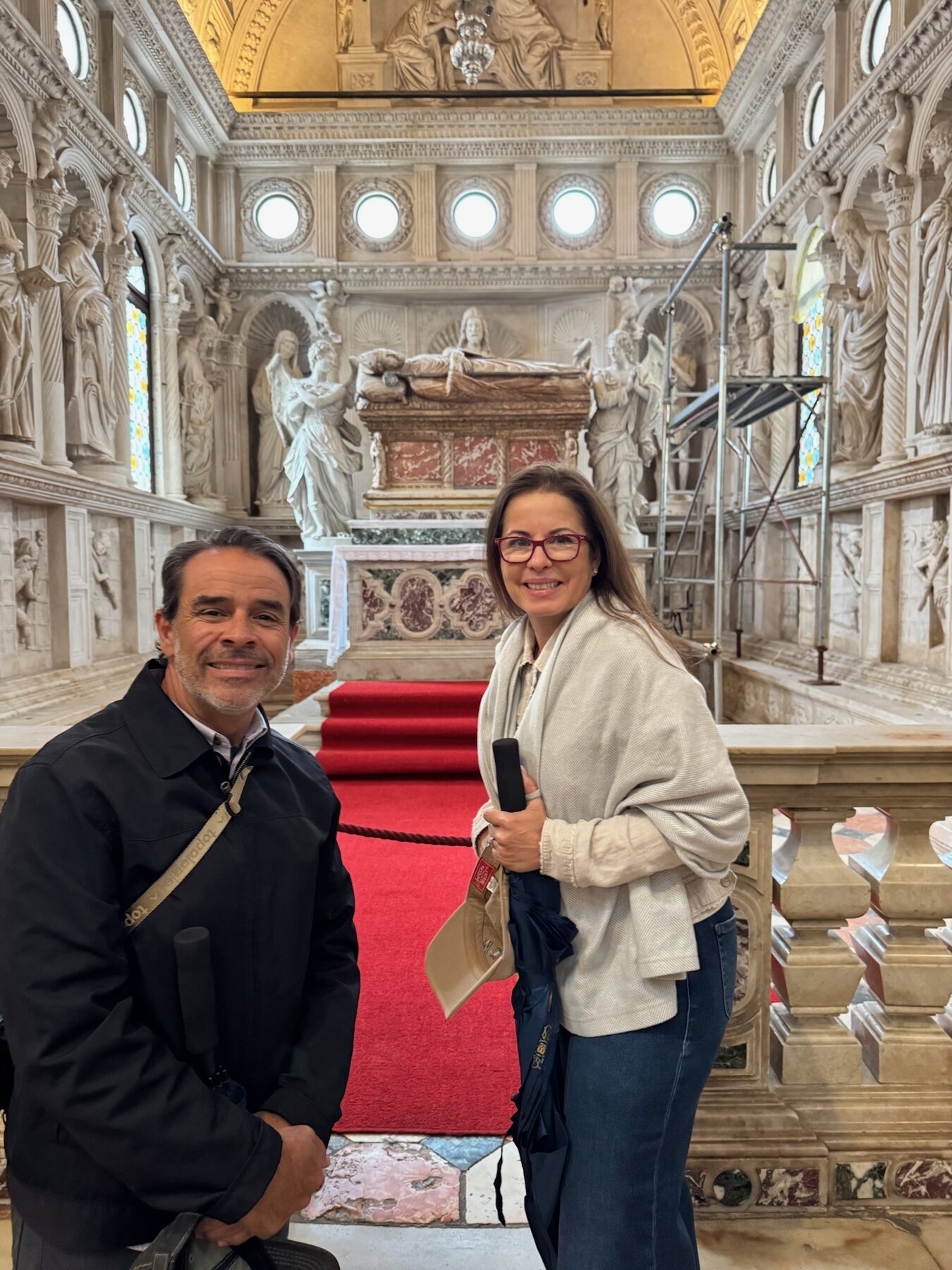 Two of our travel companions smiling in front of the carved marble chapel and red carpet in Trogir cathedral