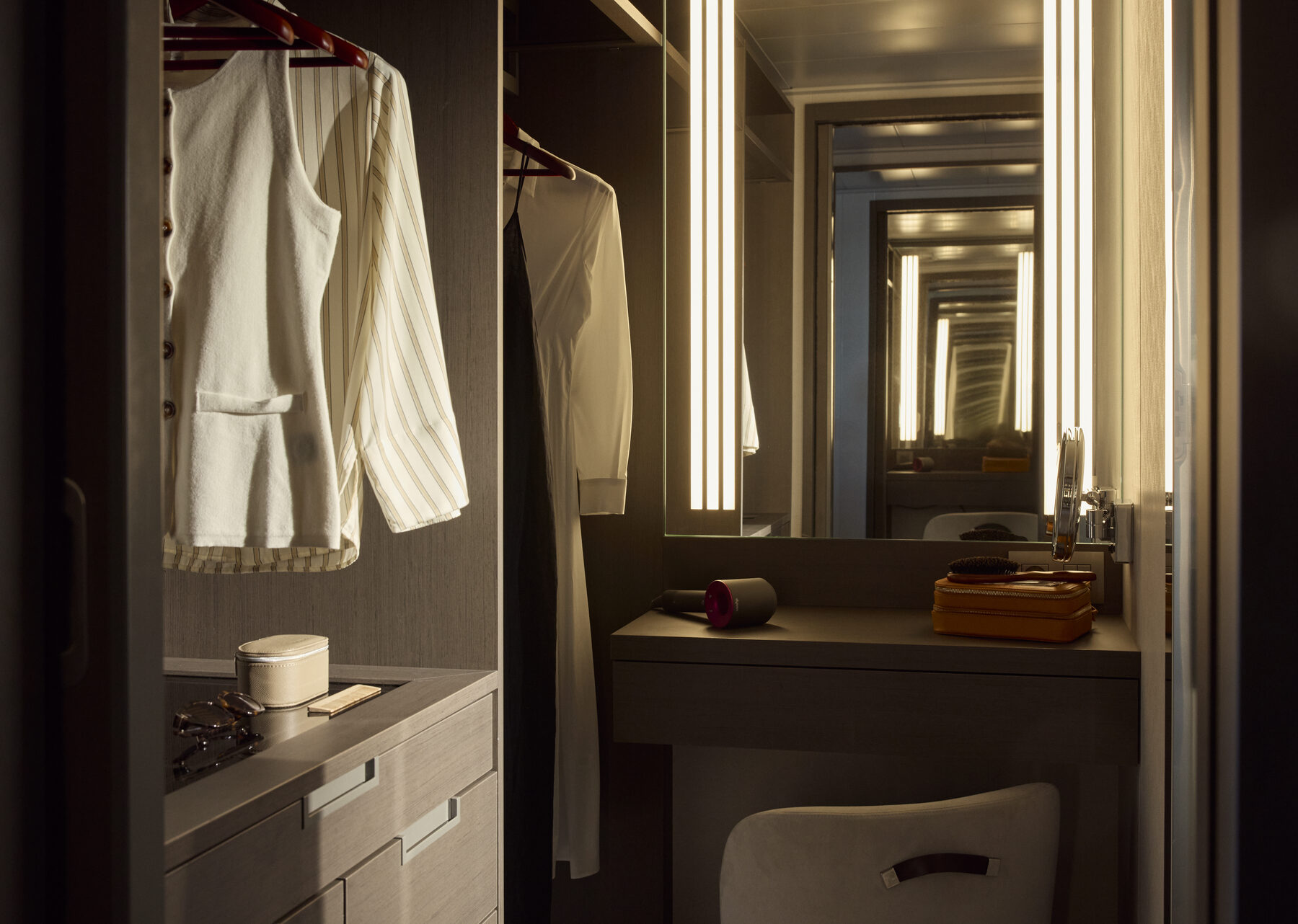 Explora media kit photo of a stateroom dressing area with vanity, lit mirror, and closet hung with robes