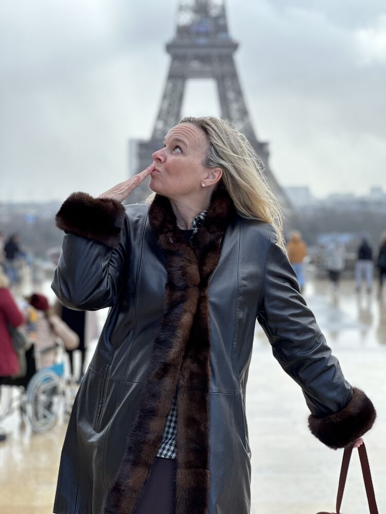 A woman in a long coat posing in front of the Eiffel Tower