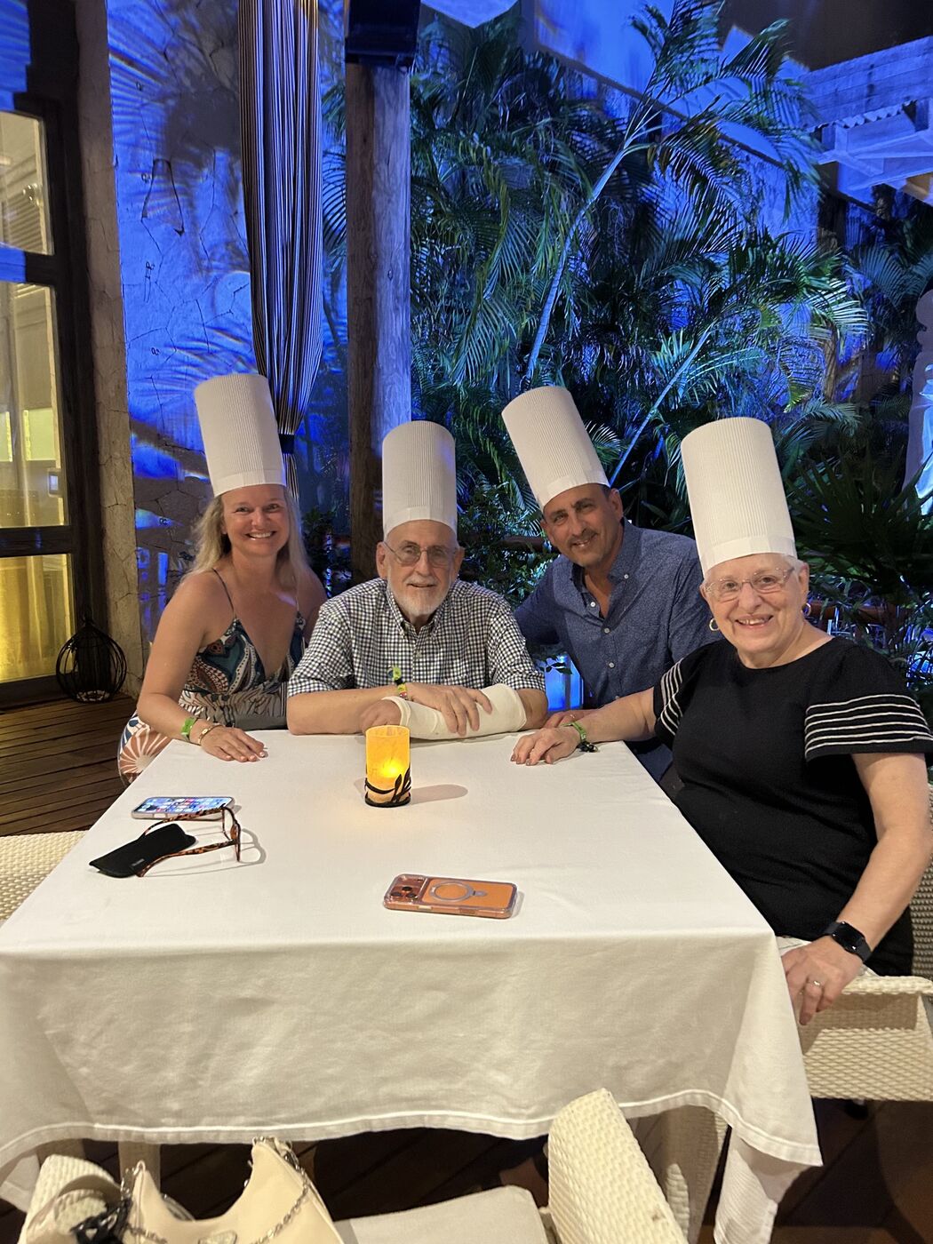 She-Stache, He-Stache&rsquo;s dad with his arm in a cast, He-Stache and He-Stache&rsquo;s mom at a candlelit table, all wearing tall paper chef hats