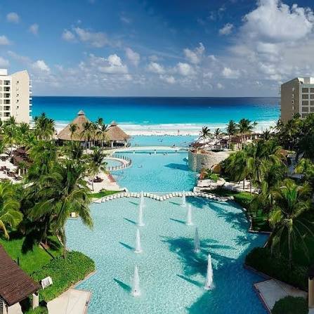 Stylized view of fountains leading to an infinity pool toward the ocean, with palapas and palms