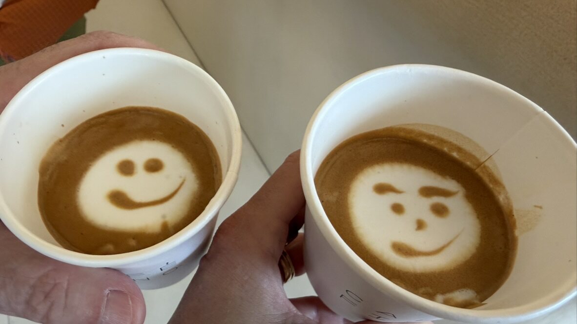 Two takeaway coffees with smiley-face latte art, one winking
