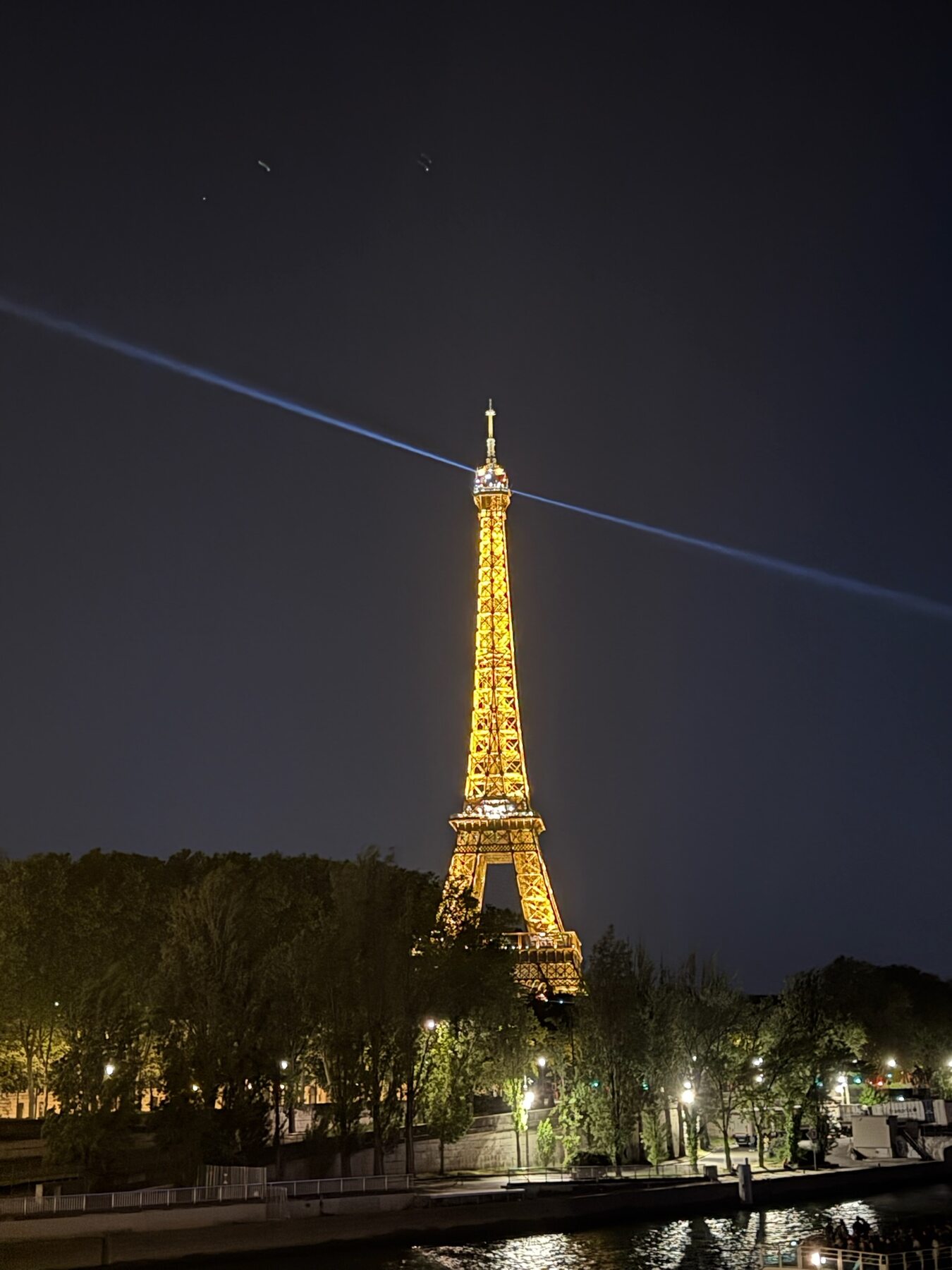 The Eiffel Tower lit gold at night with its searchlight beam sweeping across the sky
