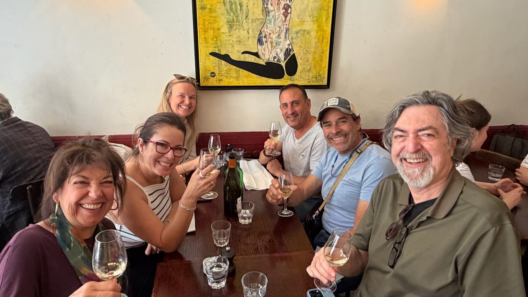 The group raising wine glasses around a table at Les Arlots under a bright yellow painting